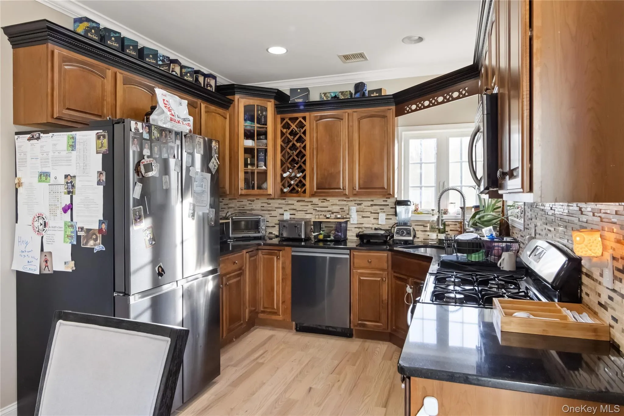 Kitchen with appliances with stainless steel finishes, glass insert cabinets, ornamental molding, dark stone counters, and light wood finished floors Kitchen with appliances with stainless steel finishes, glass insert cabinets, ornamental molding, dark stone counters, and light wood finished floors