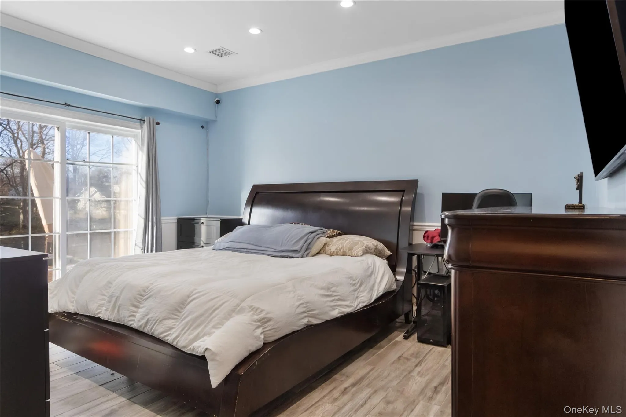 Bedroom featuring ornamental molding, light wood-style flooring, recessed lighting, and wainscoting Bedroom featuring ornamental molding, light wood-style flooring, recessed lighting, and wainscoting
