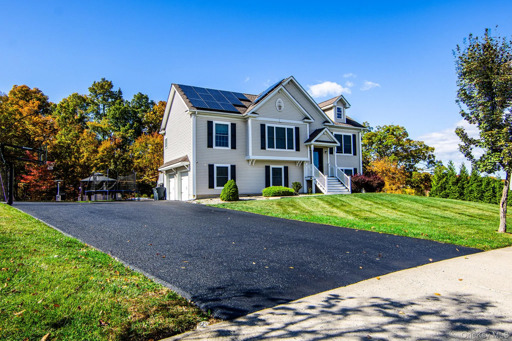 View of front of property featuring a front lawn, roof mounted solar panels, a garage, and driveway View of front of property featuring a front lawn, roof mounted solar panels, a garage, and driveway