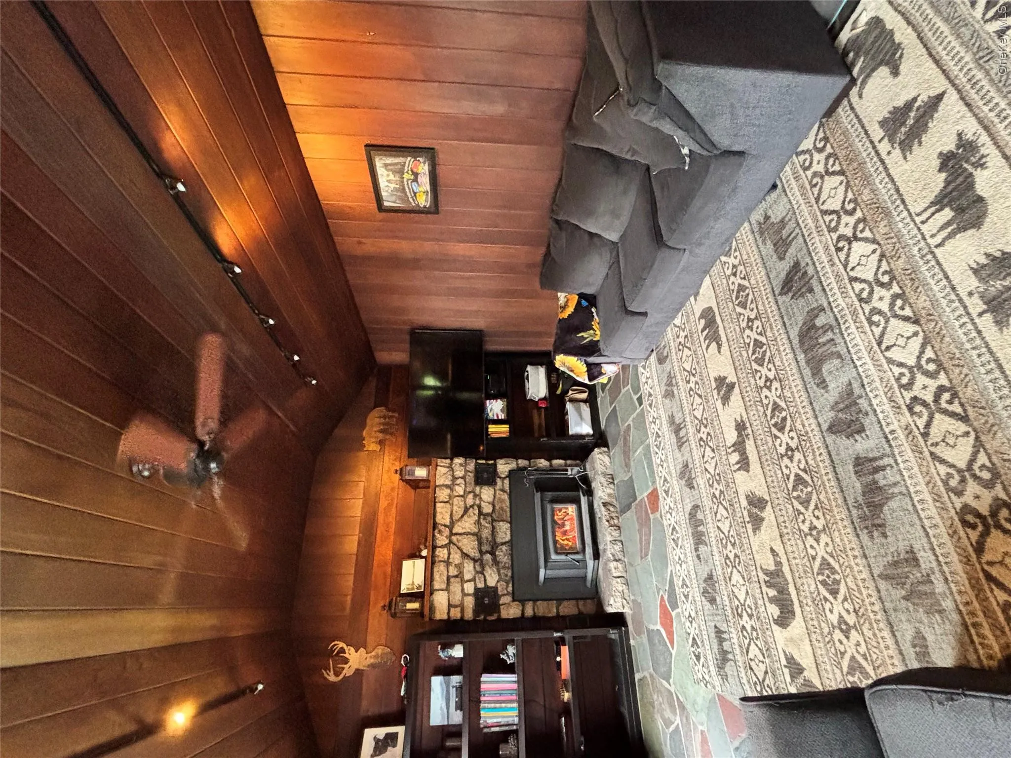 Carpeted living room with vaulted ceiling, wood walls, a ceiling fan, rail lighting, and a stone fireplace Carpeted living room with vaulted ceiling, wood walls, a ceiling fan, rail lighting, and a stone fireplace