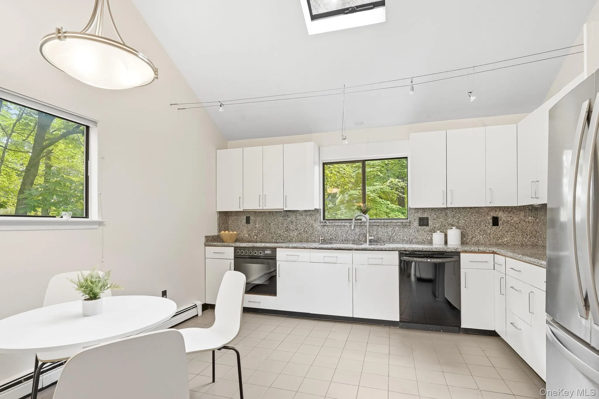 The kitchen features white cabinetry, light-toned tiled flooring, a skylight, and a stainless steel refrigerator The kitchen features white cabinetry, light-toned tiled flooring, a skylight, and a stainless steel refrigerator