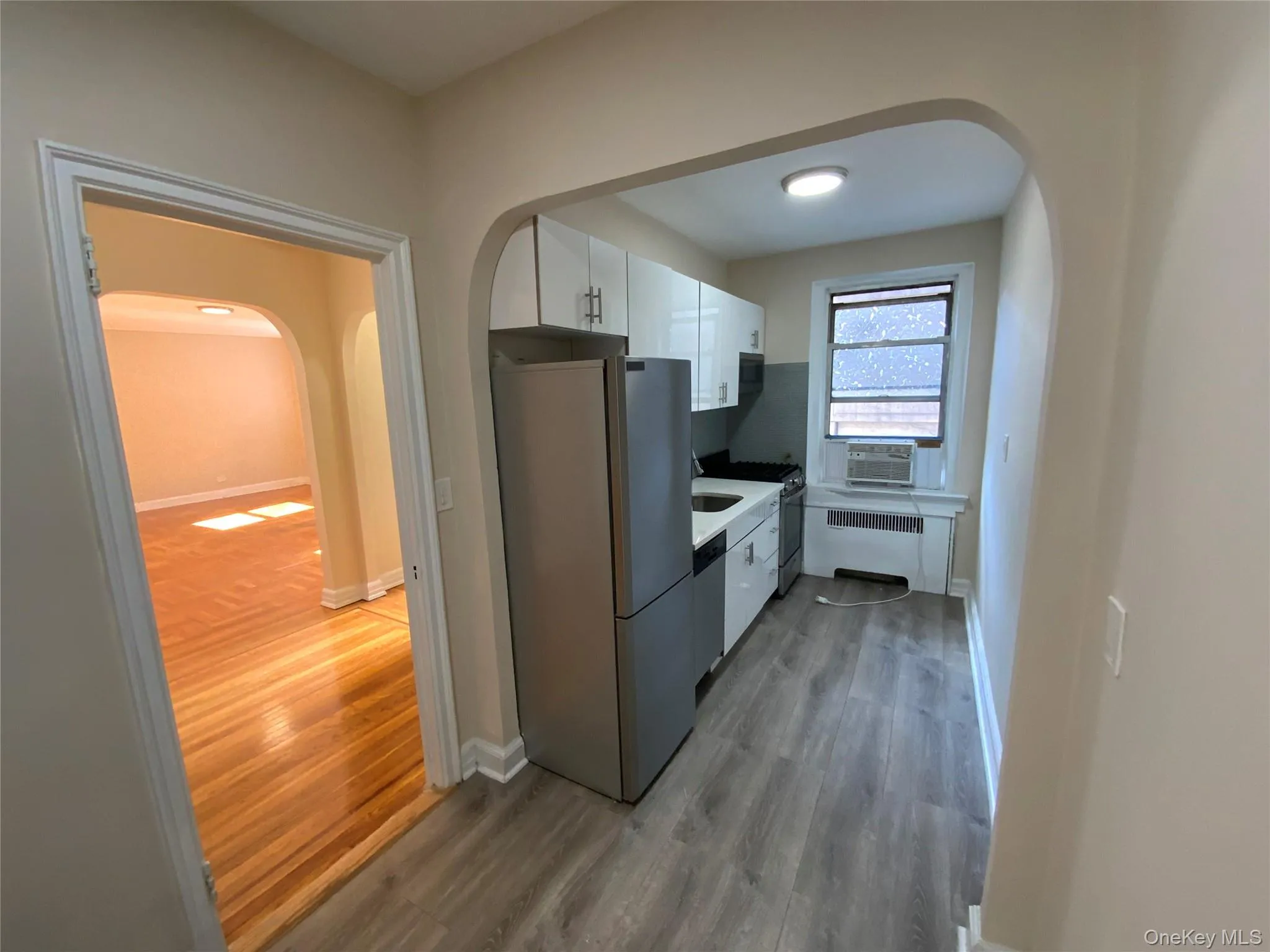 Kitchen with wood finished floors, arched walkways, white cabinetry, radiator, and appliances with stainless steel finishes Kitchen with wood finished floors, arched walkways, white cabinetry, radiator, and appliances with stainless steel finishes
