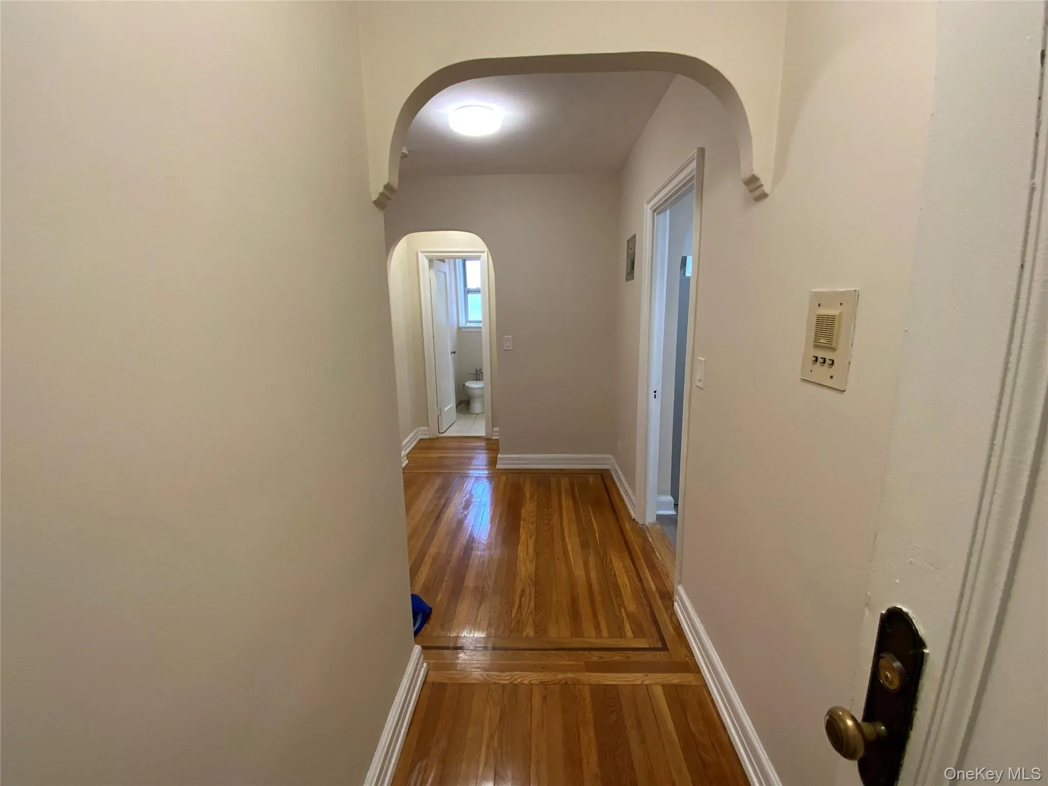 Corridor with arched walkways, wood finished floors, and baseboards Corridor with arched walkways, wood finished floors, and baseboards