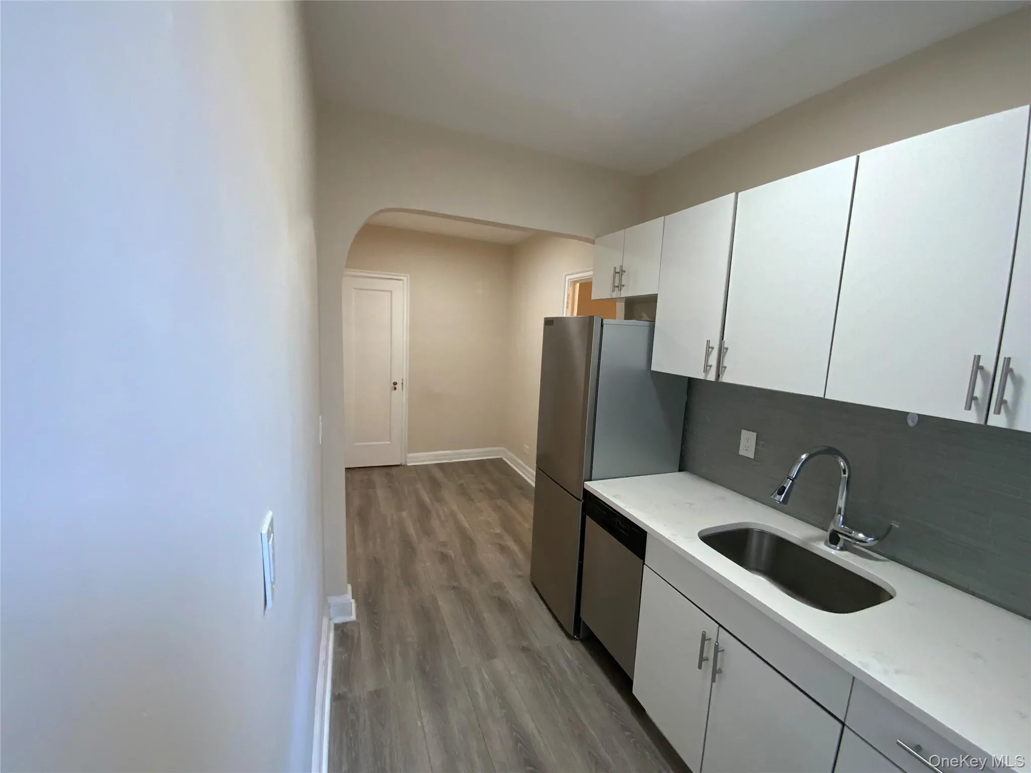 Kitchen with wood finished floors, a sink, decorative backsplash, light countertops, and appliances with stainless steel finishes Kitchen with wood finished floors, a sink, decorative backsplash, light countertops, and appliances with stainless steel finishes