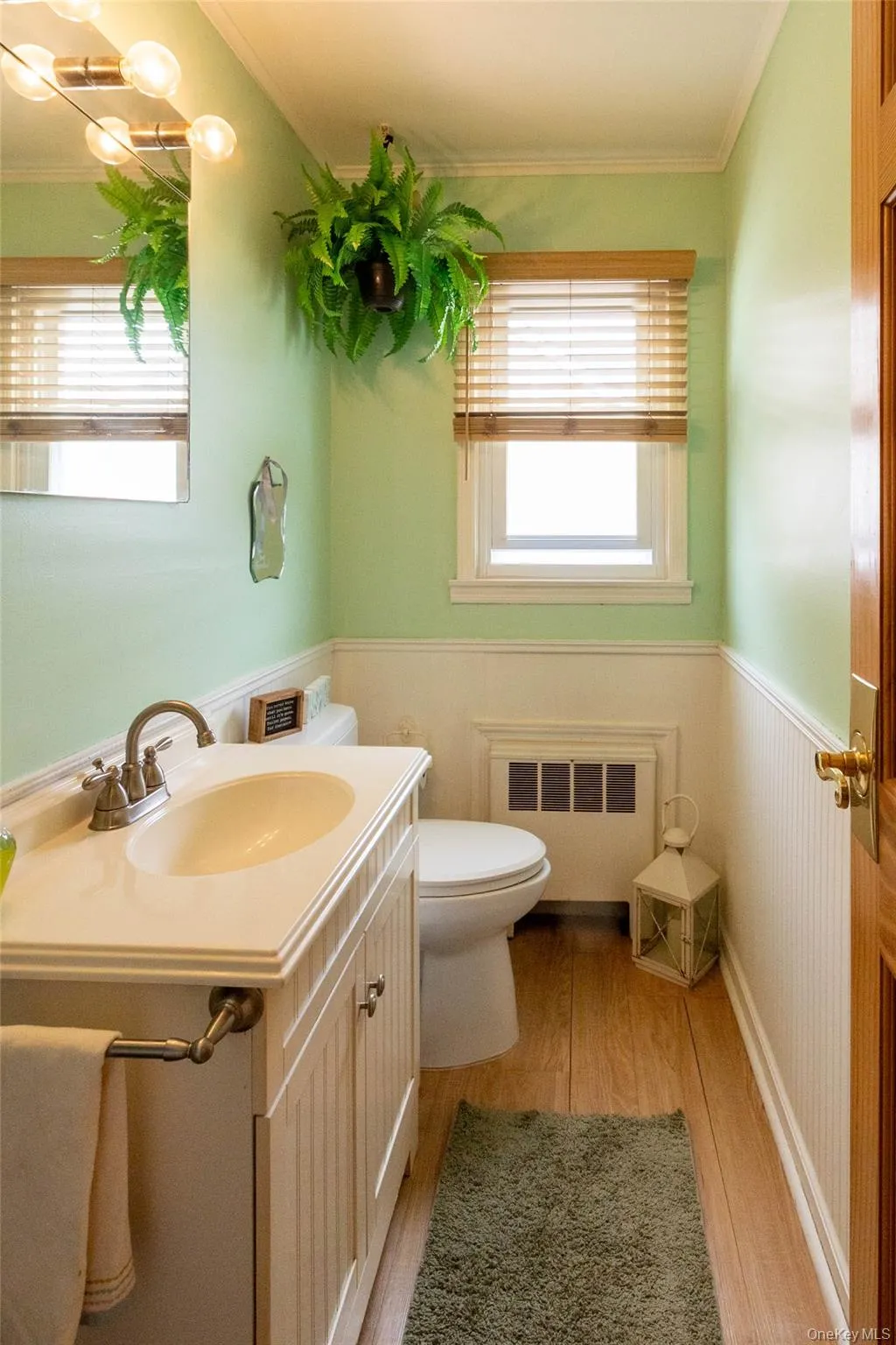 Bathroom featuring a vanity with an integrated sink, wood-finish flooring, and wainscoting Bathroom featuring a vanity with an integrated sink, wood-finish flooring, and wainscoting