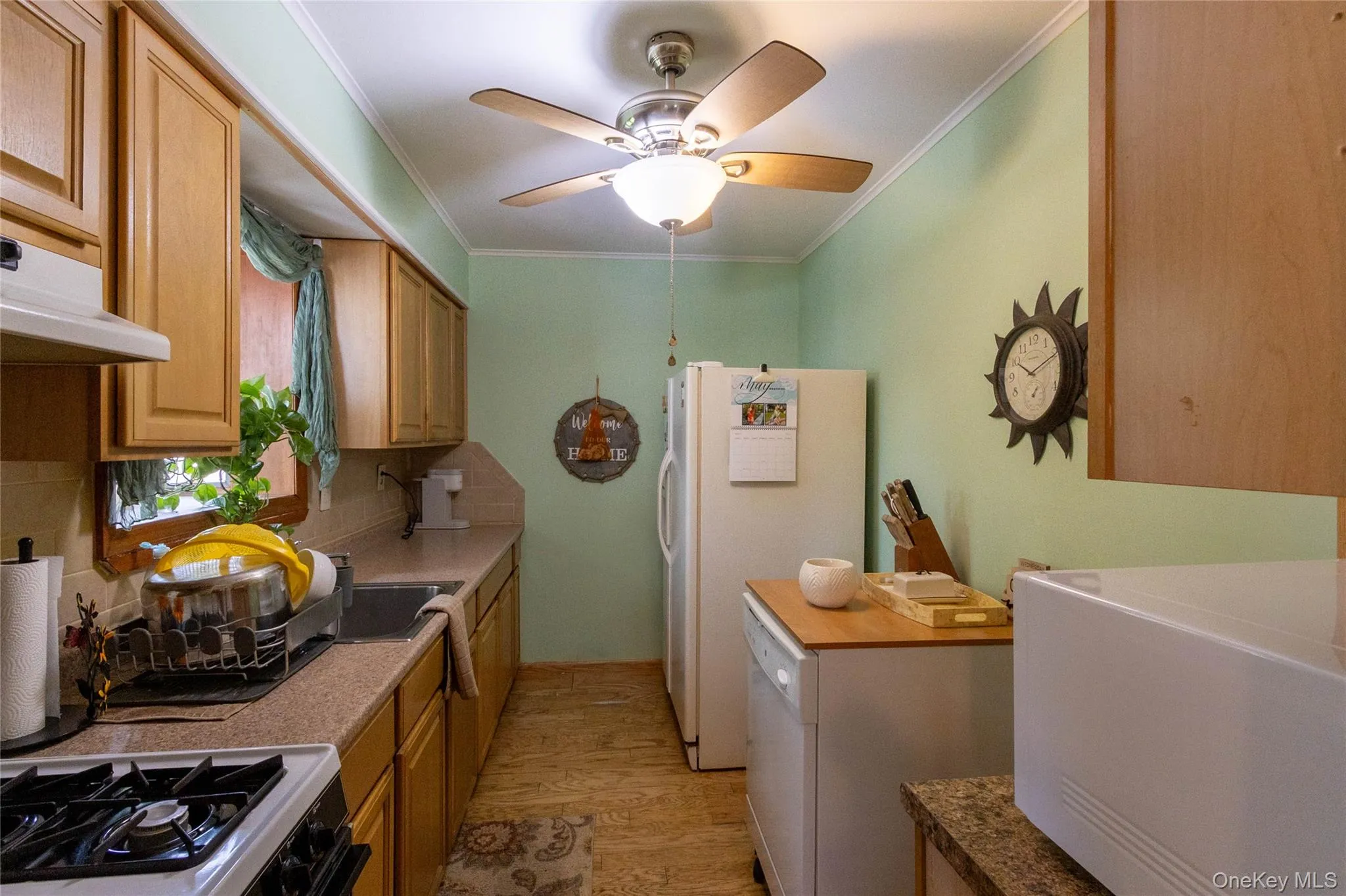 Galley kitchen featuring light wood-finish cabinetry, solid surface countertops, a stainless steel sink, and wood-finish flooring Galley kitchen featuring light wood-finish cabinetry, solid surface countertops, a stainless steel sink, and wood-finish flooring
