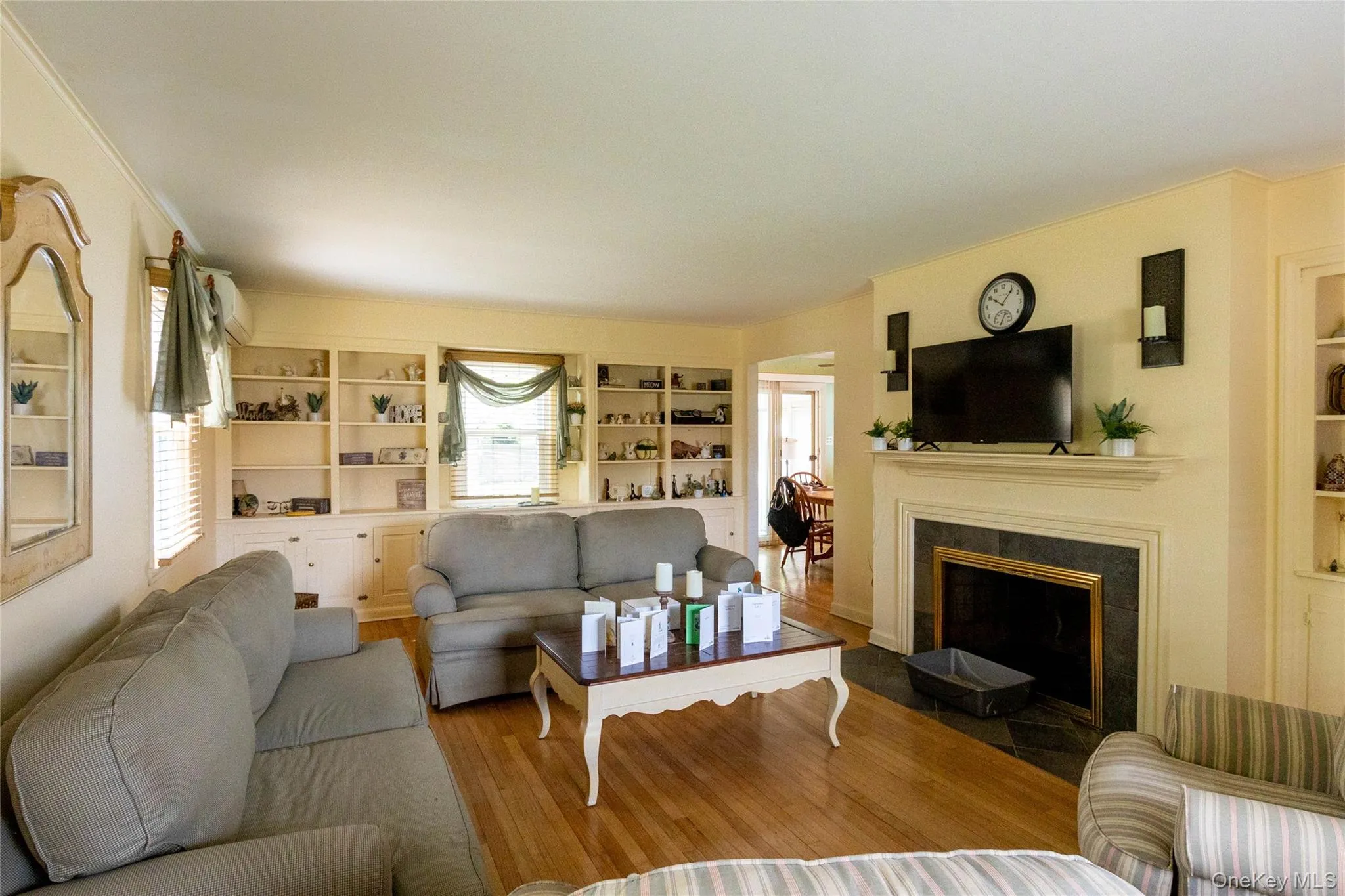 Living room featuring hardwood flooring, built-in shelving, a fireplace with a dark stone surround, and crown molding Living room featuring hardwood flooring, built-in shelving, a fireplace with a dark stone surround, and crown molding