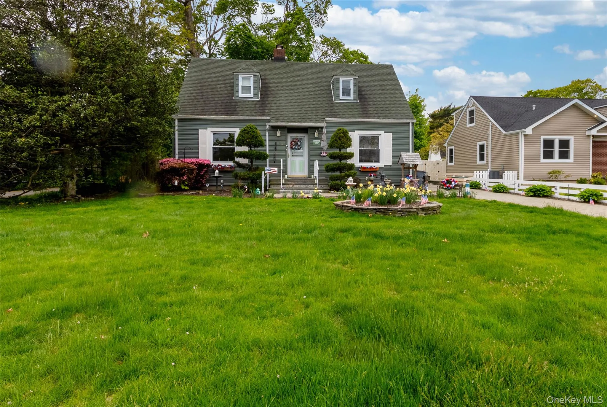 Gray siding exterior with white window shutters, a front entry door, and a dark shingle roof with two dormer windows Gray siding exterior with white window shutters, a front entry door, and a dark shingle roof with two dormer windows