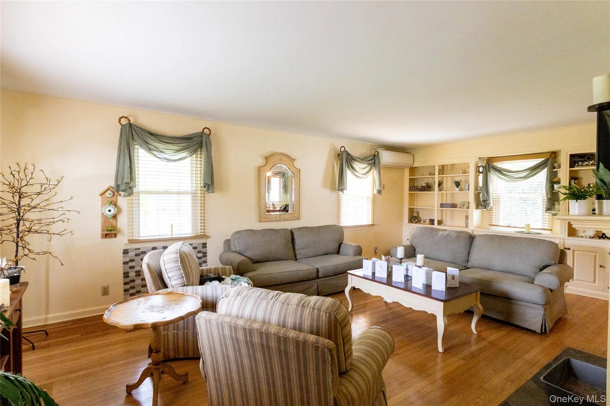 Living area with hardwood flooring, multiple windows, built-in shelving, and light-toned walls Living area with hardwood flooring, multiple windows, built-in shelving, and light-toned walls