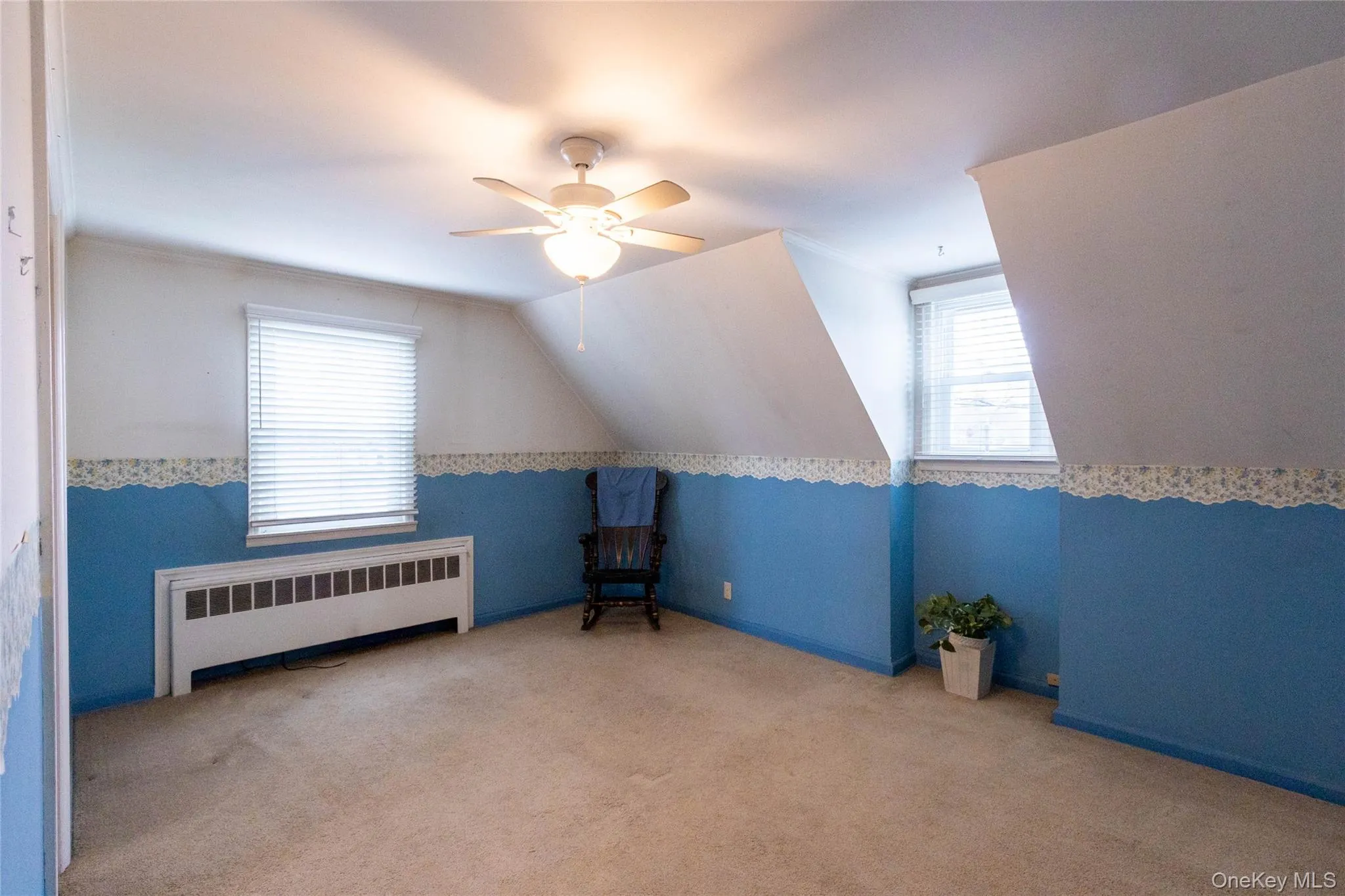 Carpeted room featuring a ceiling fan with integrated lighting, two windows with horizontal blinds, an integrated heating unit, and sloped ceiling details Carpeted room featuring a ceiling fan with integrated lighting, two windows with horizontal blinds, an integrated heating unit, and sloped ceiling details