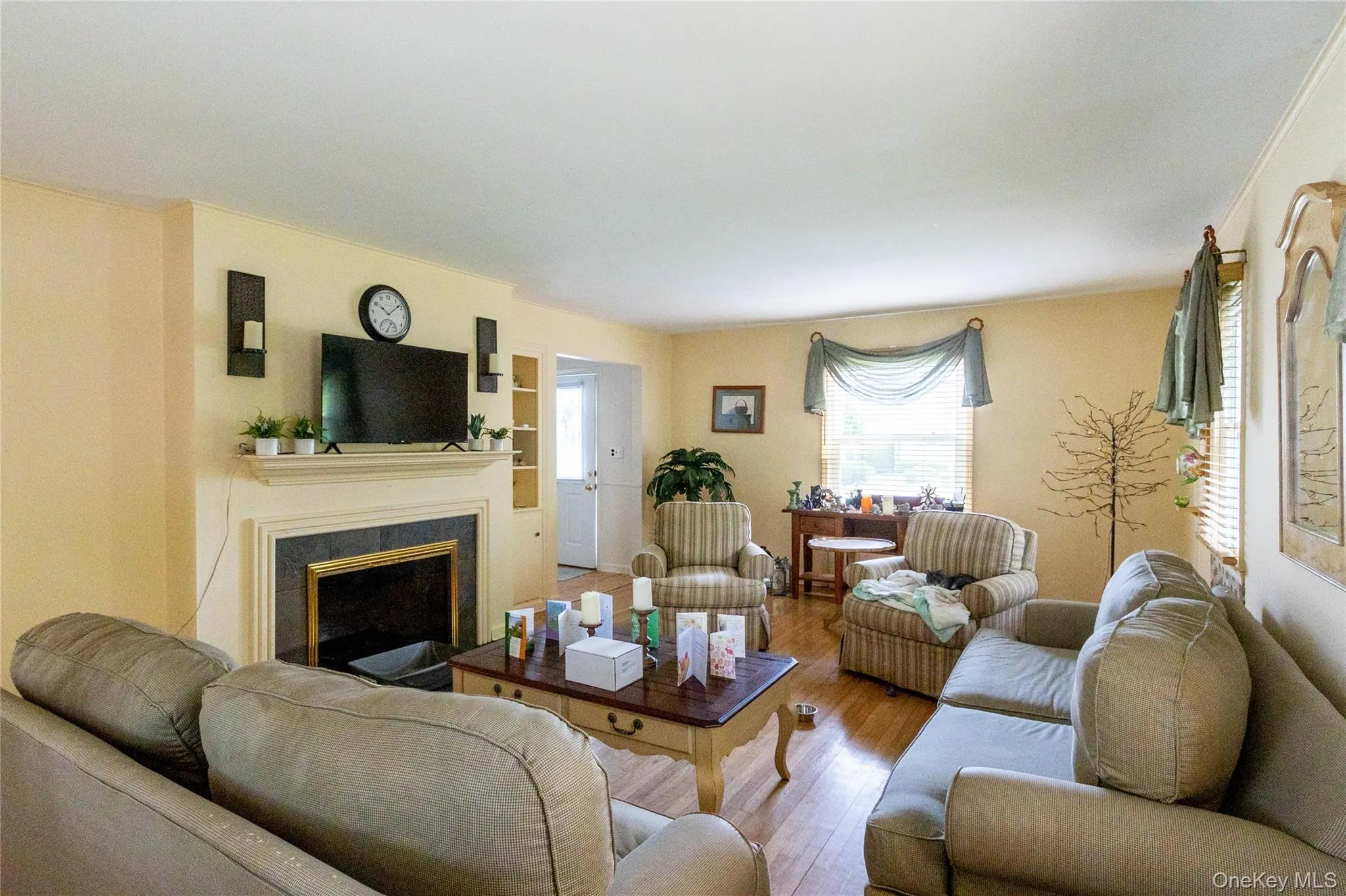 Spacious living area featuring warm-toned walls, wood-finish flooring, a fireplace with a black surround and white mantel, and built-in shelving Spacious living area featuring warm-toned walls, wood-finish flooring, a fireplace with a black surround and white mantel, and built-in shelving