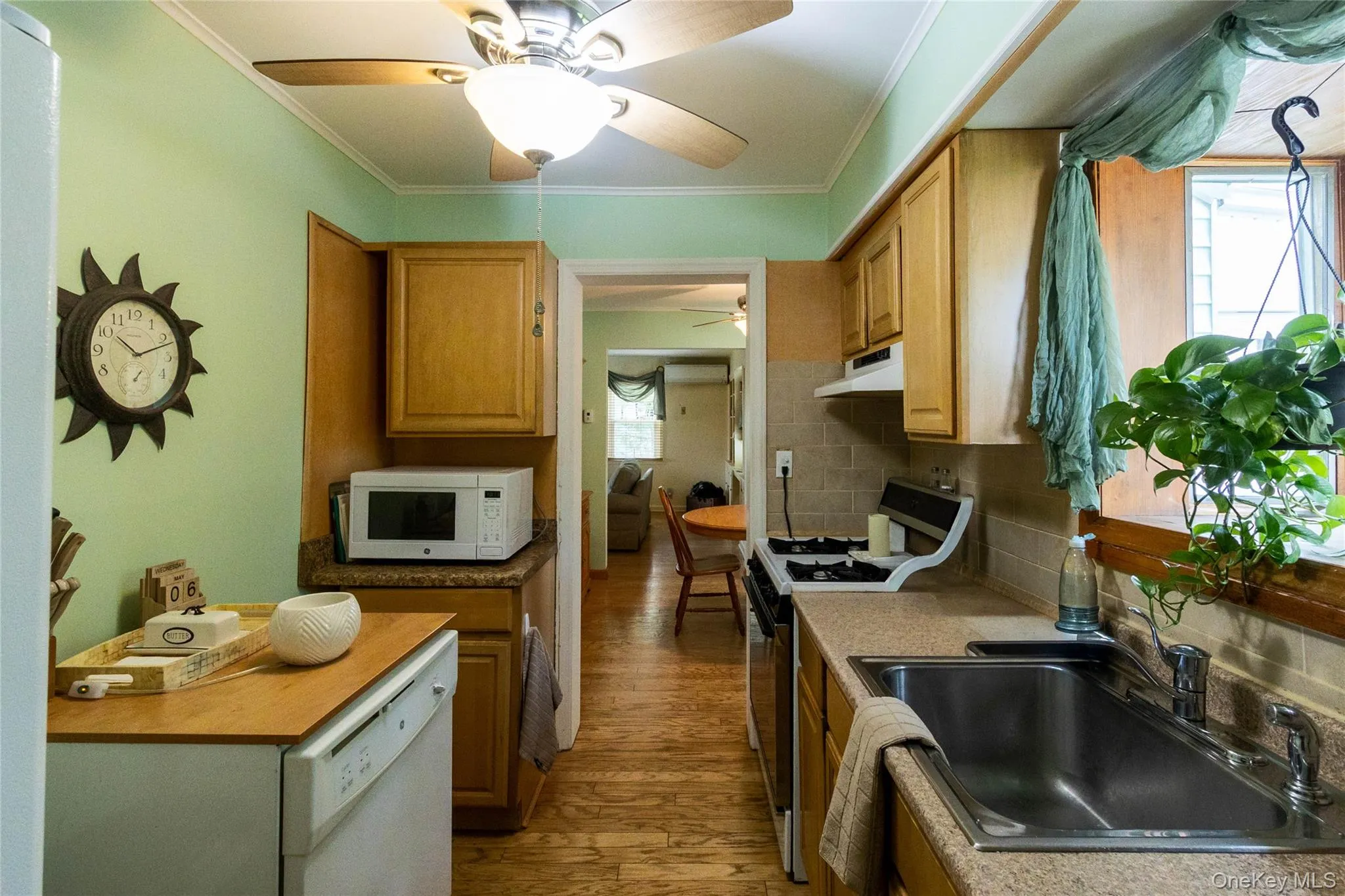 Galley kitchen featuring wood-finish flooring, wood cabinetry, light-toned countertops, and a stainless steel sink Galley kitchen featuring wood-finish flooring, wood cabinetry, light-toned countertops, and a stainless steel sink