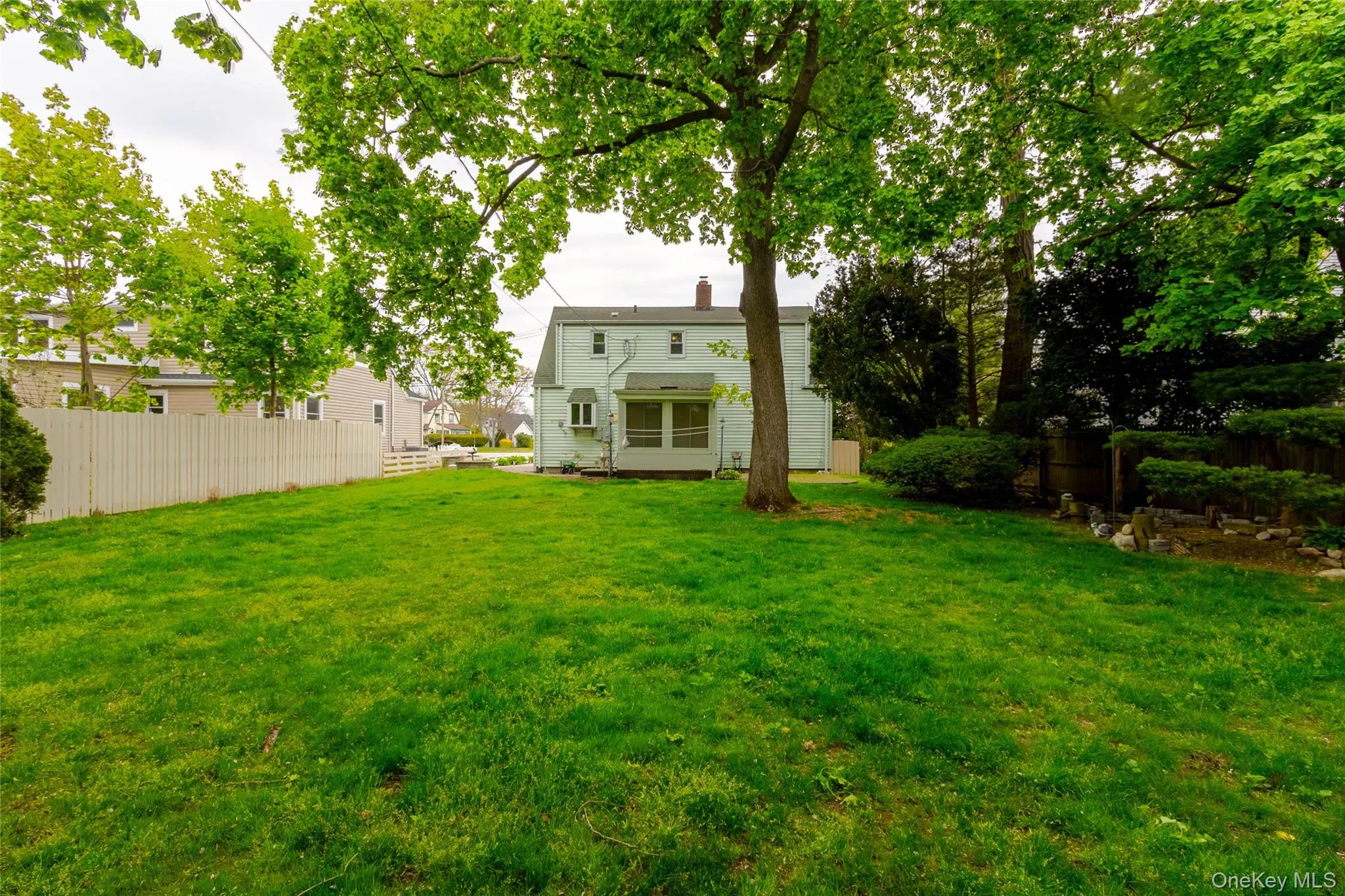 Expansive rear yard featuring a large verdant lawn, mature trees, and a white picket fence Expansive rear yard featuring a large verdant lawn, mature trees, and a white picket fence