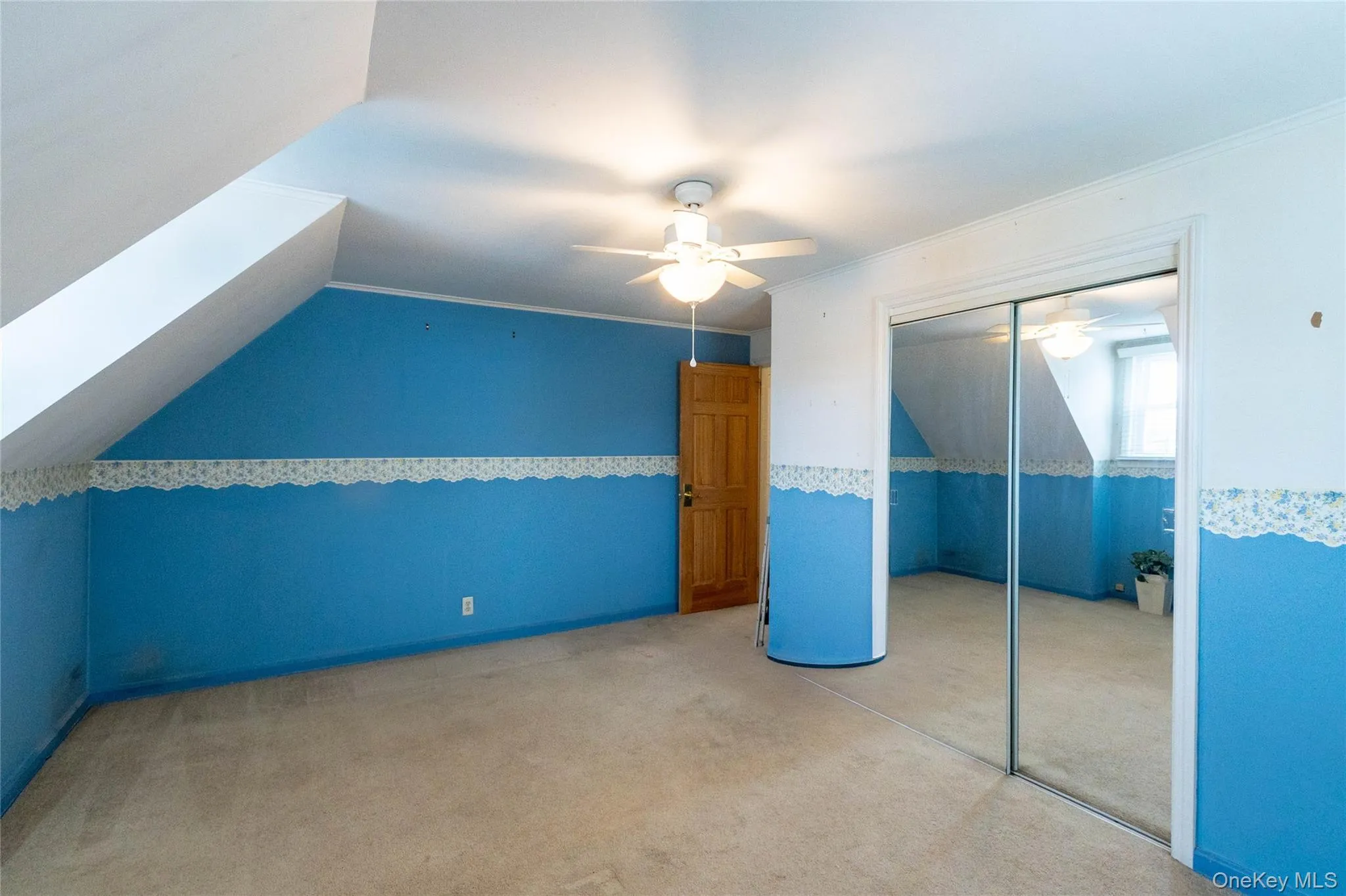 Attic room featuring sloped ceilings, a ceiling fan with light fixture, mirrored closet doors, and carpeted flooring Attic room featuring sloped ceilings, a ceiling fan with light fixture, mirrored closet doors, and carpeted flooring