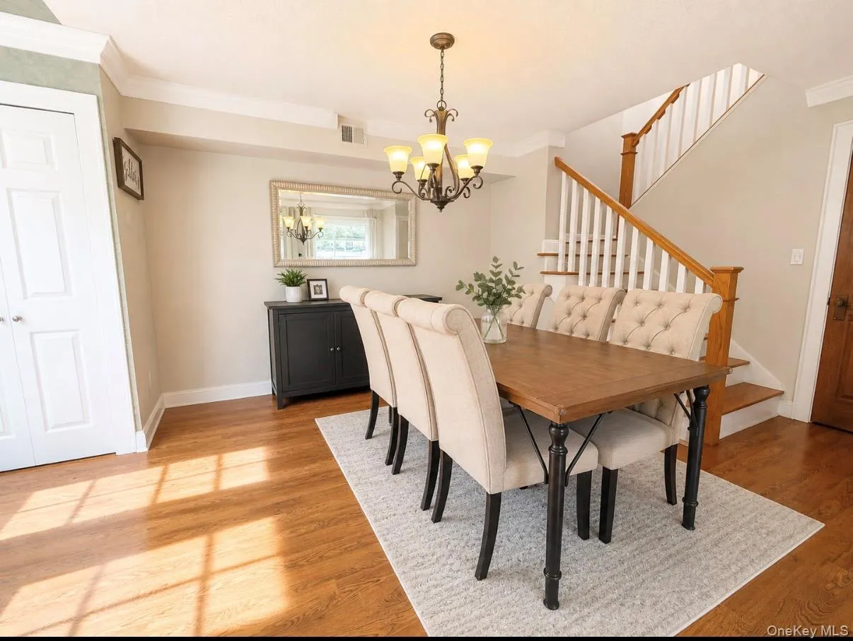 Dining area featuring wood-finish flooring, a traditional chandelier, crown molding, and a staircase with white spindles and wood handrails Dining area featuring wood-finish flooring, a traditional chandelier, crown molding, and a staircase with white spindles and wood handrails