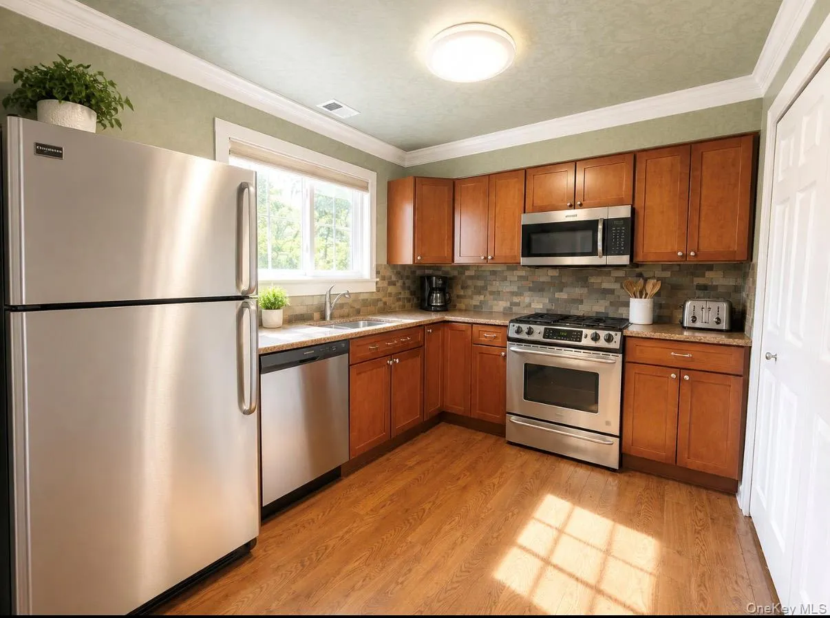 Kitchen featuring wood-finish flooring, stainless steel appliances, wood cabinetry, and a tile backsplash Kitchen featuring wood-finish flooring, stainless steel appliances, wood cabinetry, and a tile backsplash