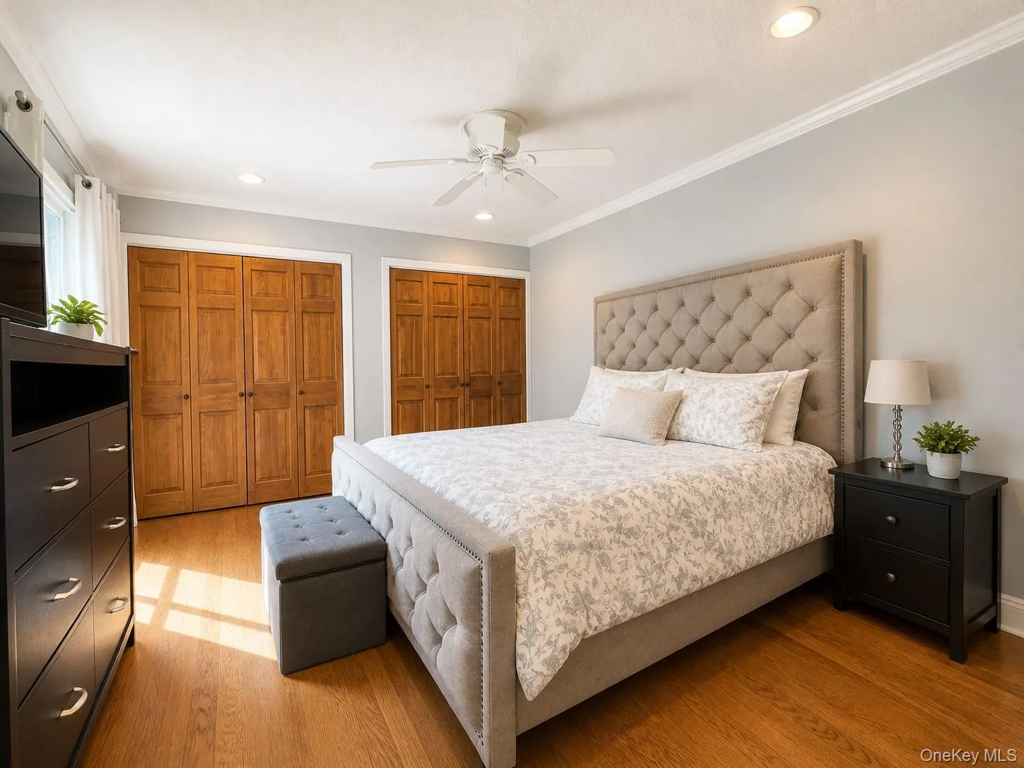 Bedroom featuring hardwood flooring, crown molding, recessed lighting, a ceiling fan, and two sets of bi-fold wooden closet doors Bedroom featuring hardwood flooring, crown molding, recessed lighting, a ceiling fan, and two sets of bi-fold wooden closet doors