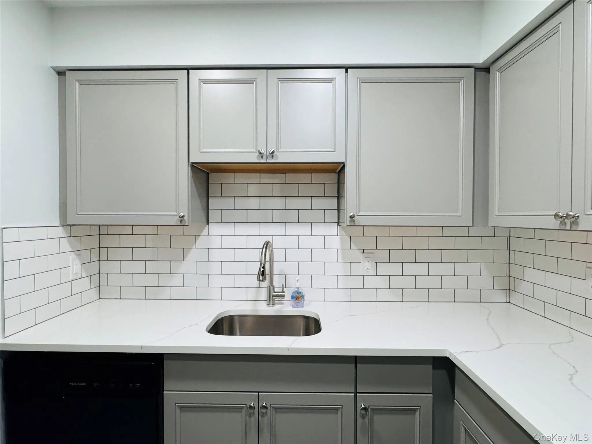 Kitchen featuring light gray cabinetry with chrome hardware, white subway tile backsplash, white quartz countertop with gray veining. Kitchen featuring light gray cabinetry with chrome hardware, white subway tile backsplash, white quartz countertop with gray veining.