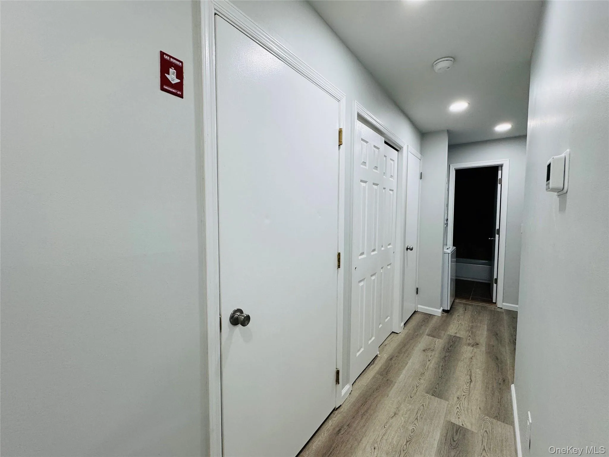 Hallway featuring vinyl wood-style flooring, recessed lighting, white panel doors, and a neutral grey wall palette. Features utility closet and large closet for storage. Hallway featuring vinyl wood-style flooring, recessed lighting, white panel doors, and a neutral grey wall palette. Features utility closet and large closet for storage.