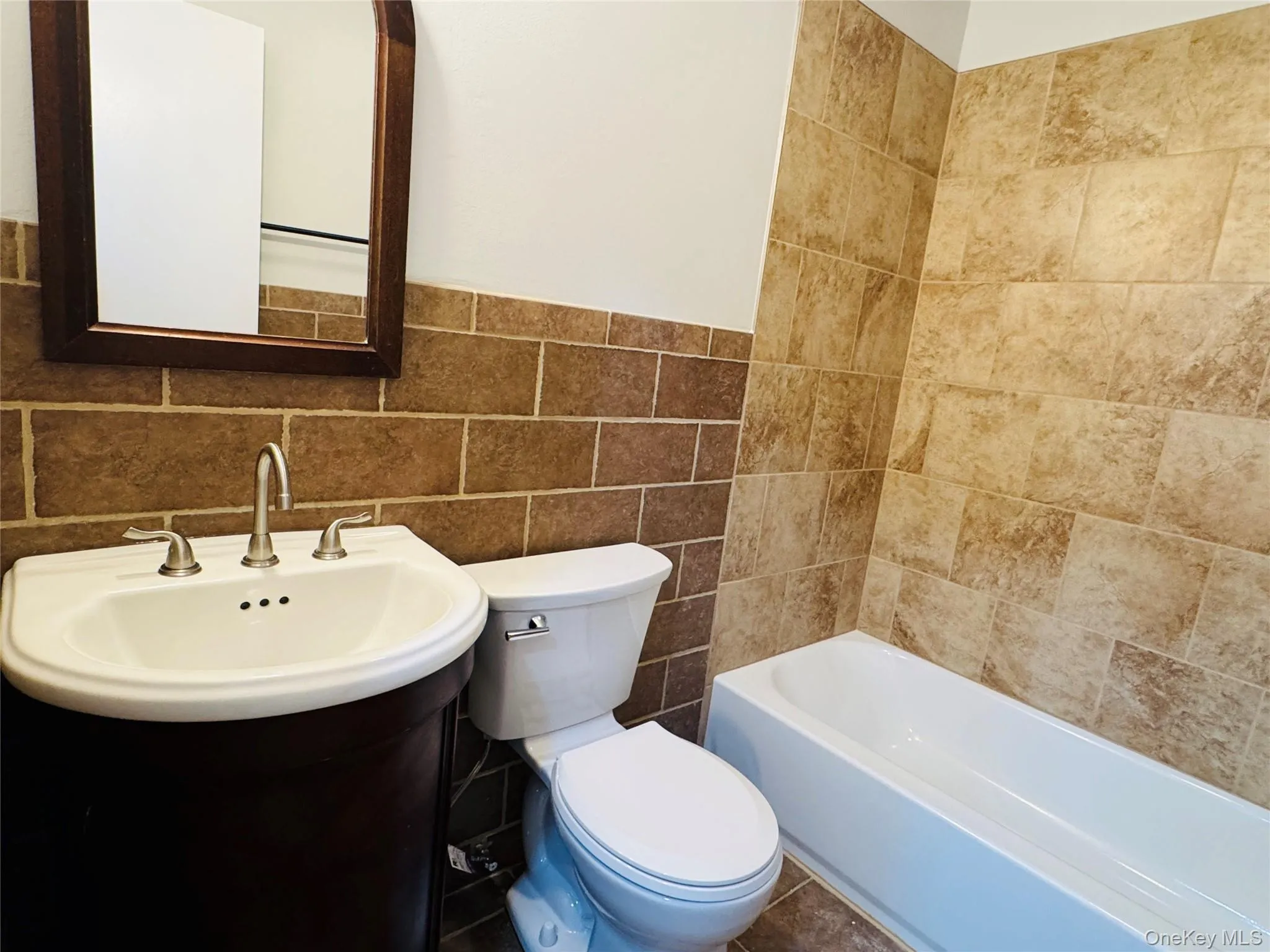 Bathroom featuring a sink with brushed nickel faucet, a white toilet, and a white bathtub with subway tile walls. Bathroom featuring a sink with brushed nickel faucet, a white toilet, and a white bathtub with subway tile walls.