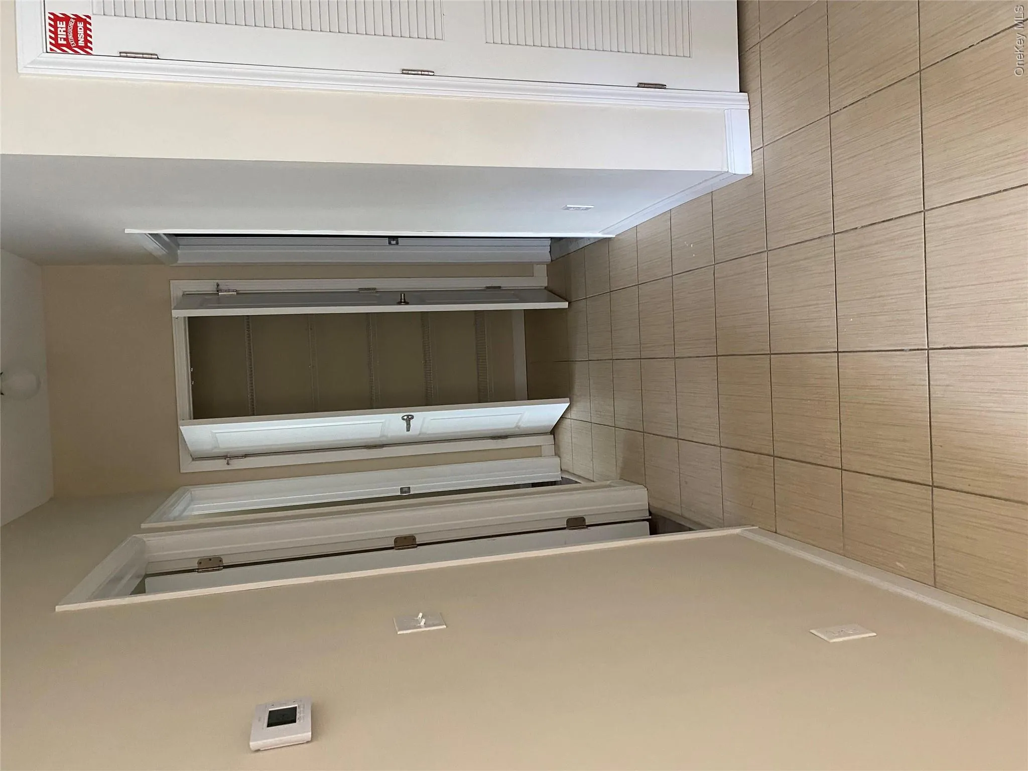 Tiled hallway featuring a built-in closet with shelving, multiple doors, and a wall-mounted thermostat Tiled hallway featuring a built-in closet with shelving, multiple doors, and a wall-mounted thermostat