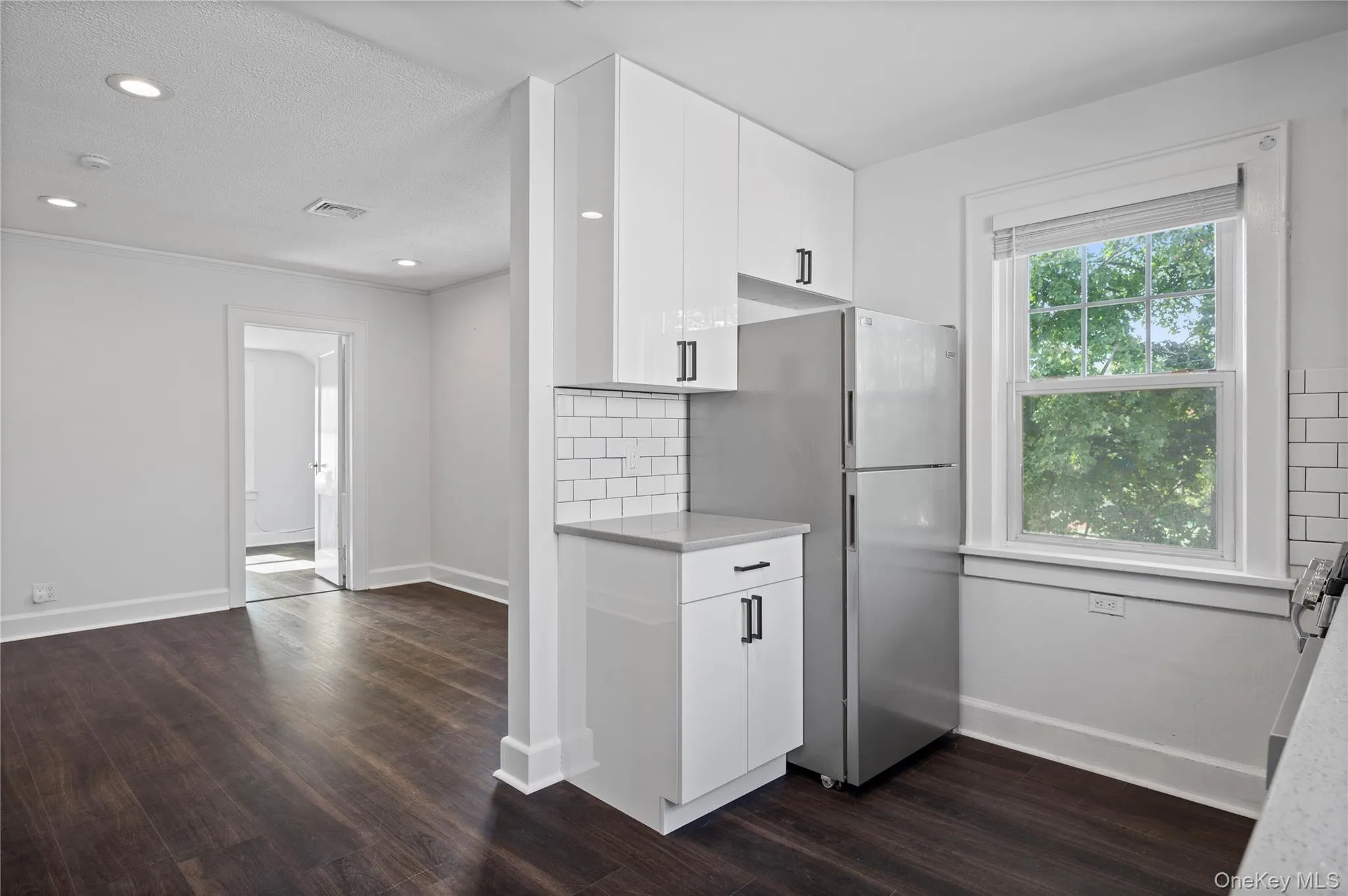 Kitchen with white cabinets, freestanding refrigerator, tasteful backsplash, dark wood-type flooring, and recessed lighting Kitchen with white cabinets, freestanding refrigerator, tasteful backsplash, dark wood-type flooring, and recessed lighting