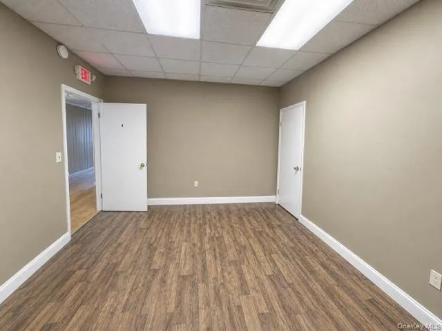 Spacious room featuring wood-finish flooring, neutral-toned walls, white trim, and a drop ceiling with recessed lighting Spacious room featuring wood-finish flooring, neutral-toned walls, white trim, and a drop ceiling with recessed lighting