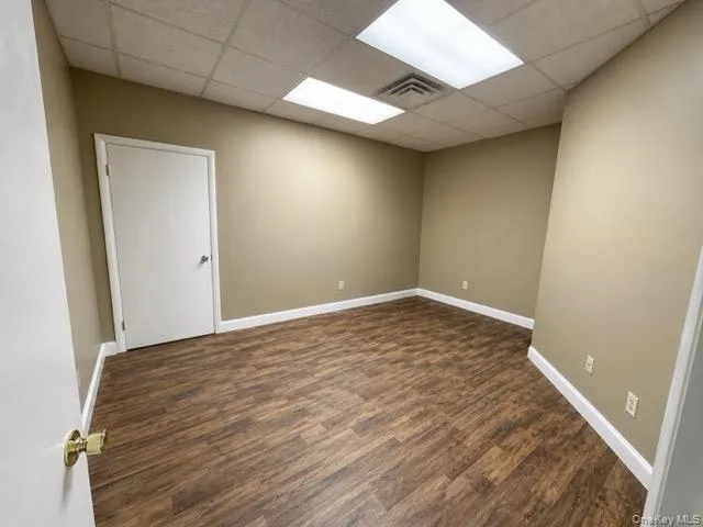 Spacious room featuring wood-finish flooring, neutral-toned walls, white baseboards, and a drop ceiling with recessed lighting Spacious room featuring wood-finish flooring, neutral-toned walls, white baseboards, and a drop ceiling with recessed lighting