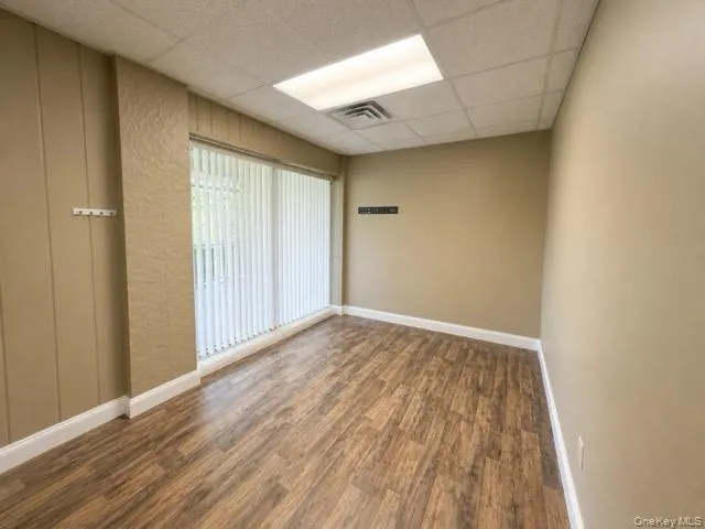 Room featuring wood-finish flooring, vertical blinds, and a suspended acoustic ceiling with recessed lighting Room featuring wood-finish flooring, vertical blinds, and a suspended acoustic ceiling with recessed lighting