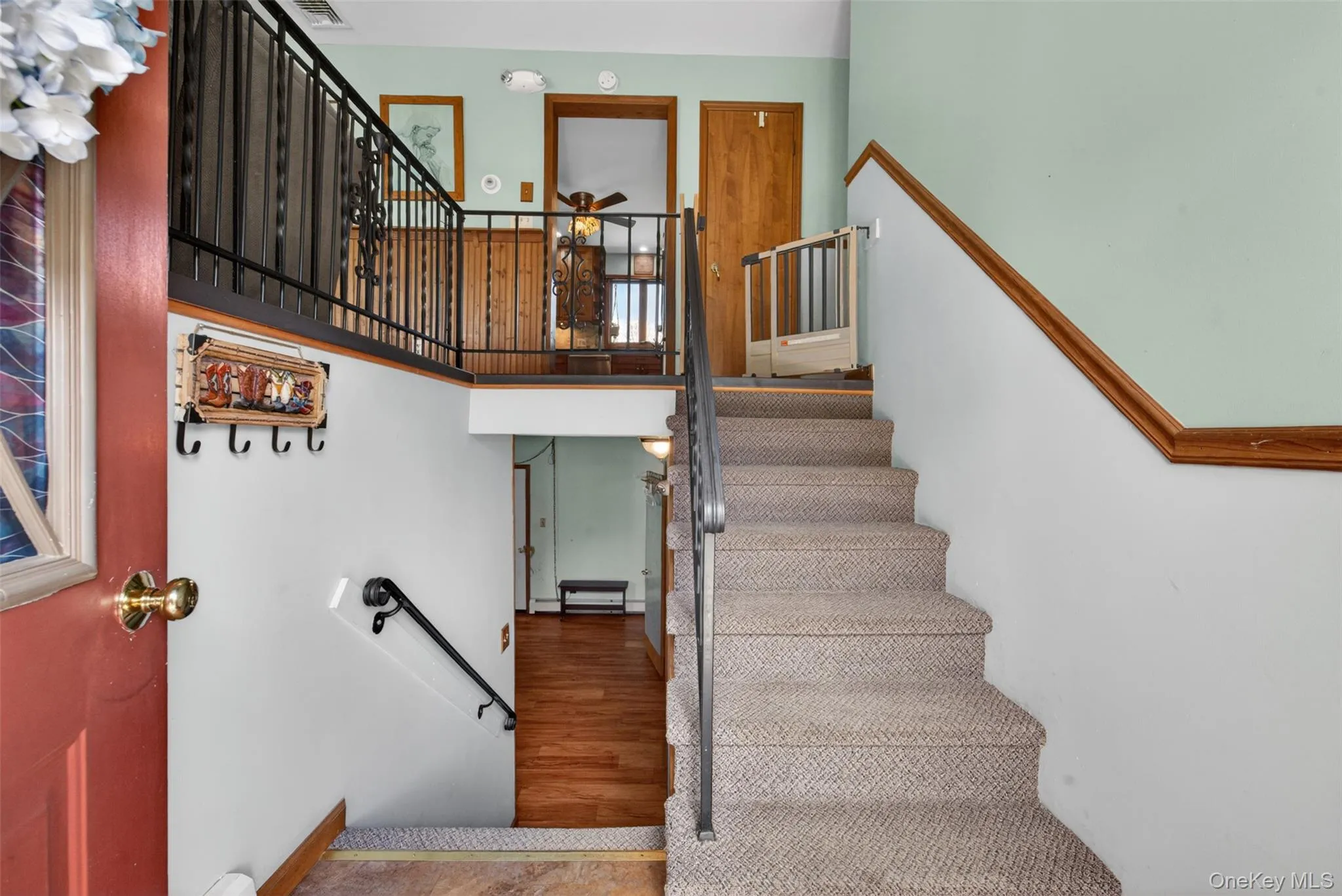 Multi-level entryway featuring carpeted stairs with a metal handrail, wood-finish flooring, and light green wall accents Multi-level entryway featuring carpeted stairs with a metal handrail, wood-finish flooring, and light green wall accents
