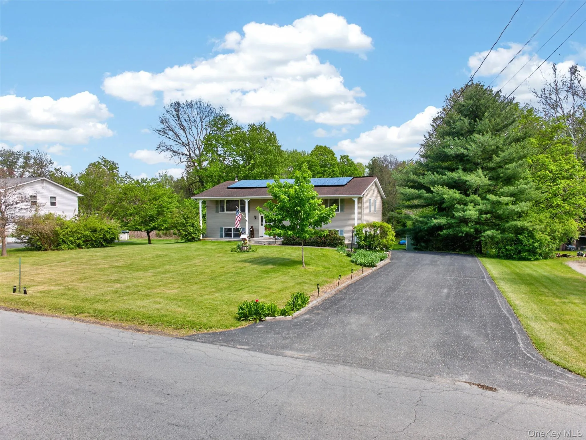 Split-level residence featuring a paved driveway, front porch with columns, and solar panels on the roof Split-level residence featuring a paved driveway, front porch with columns, and solar panels on the roof