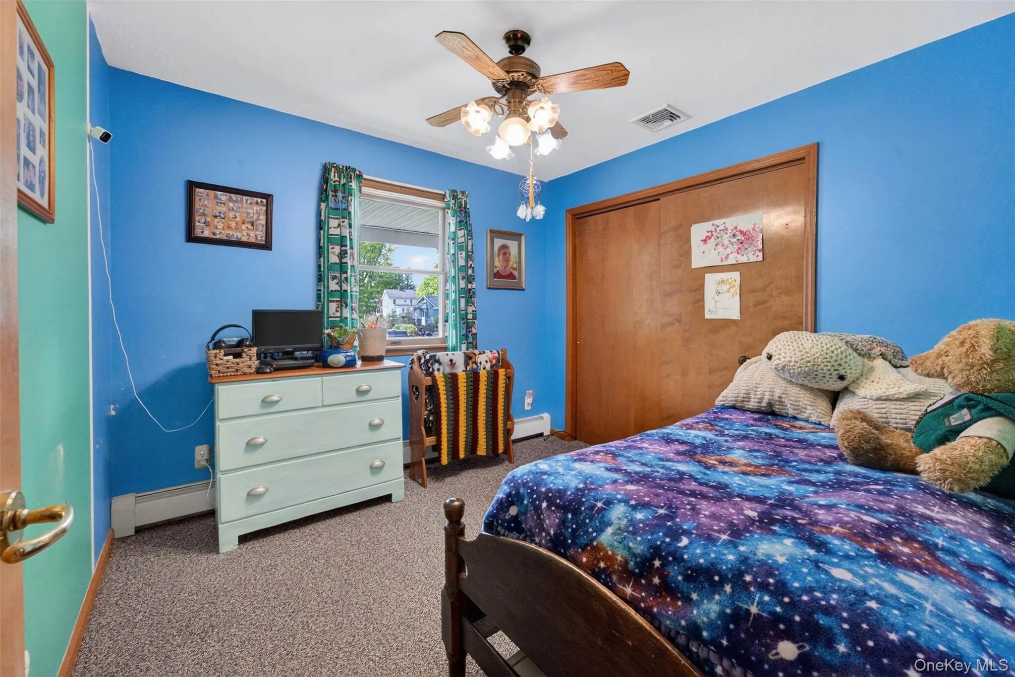 Carpeted room featuring a ceiling fan, a window with exterior views, a wood-finish door, and baseboard heating Carpeted room featuring a ceiling fan, a window with exterior views, a wood-finish door, and baseboard heating