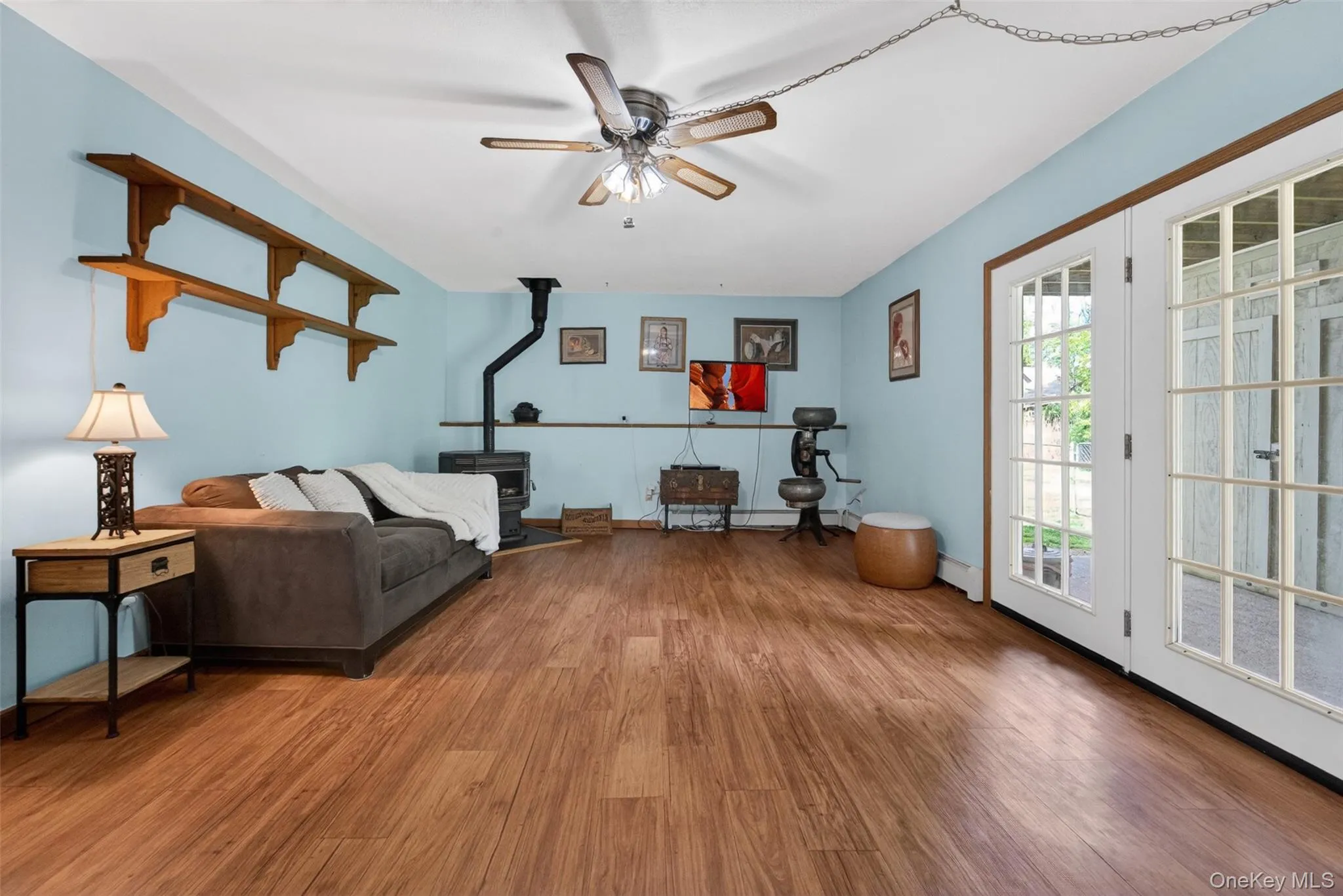 Spacious room featuring wood-finish flooring, a ceiling fan with integrated lighting, and a dark-toned Pellet stove Spacious room featuring wood-finish flooring, a ceiling fan with integrated lighting, and a dark-toned Pellet stove
