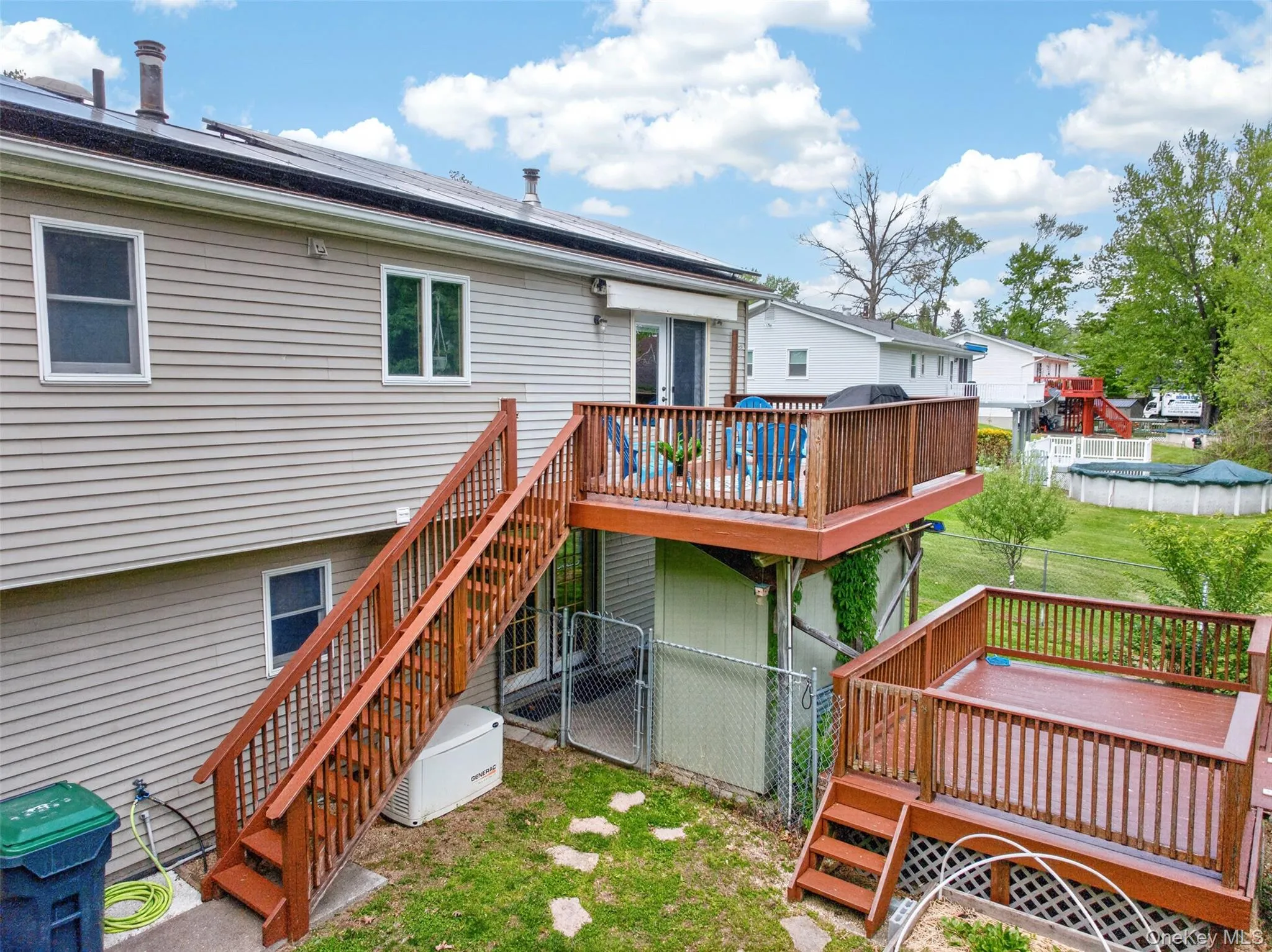 Two-tiered wood-finish deck with full railings, Full House Generator, and Green Weather Proof Pellet Storage Shed. Two-tiered wood-finish deck with full railings, Full House Generator, and Green Weather Proof Pellet Storage Shed.