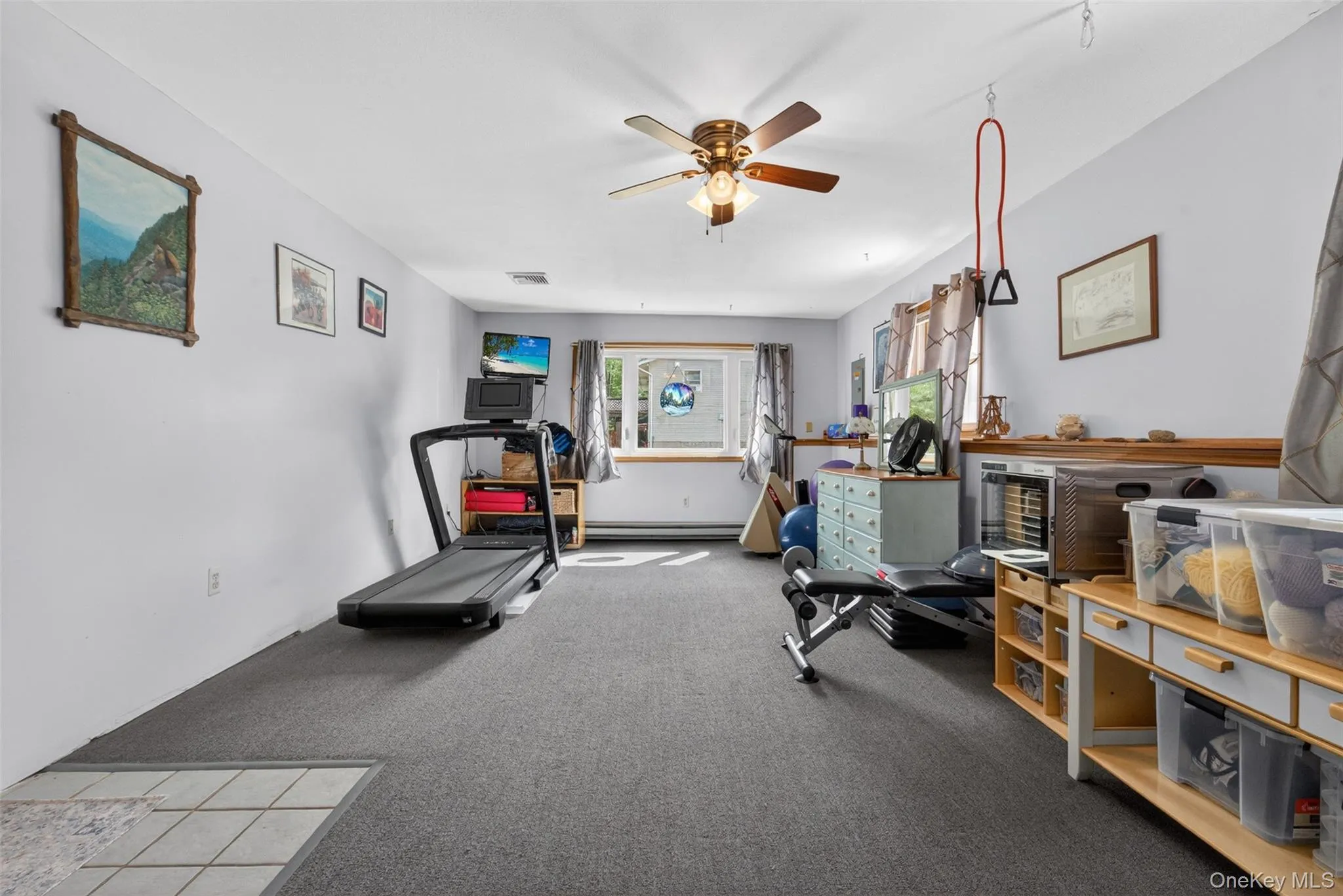 Spacious room featuring gray carpeting, light gray walls, a ceiling fan with integrated lighting, and multiple windows Spacious room featuring gray carpeting, light gray walls, a ceiling fan with integrated lighting, and multiple windows