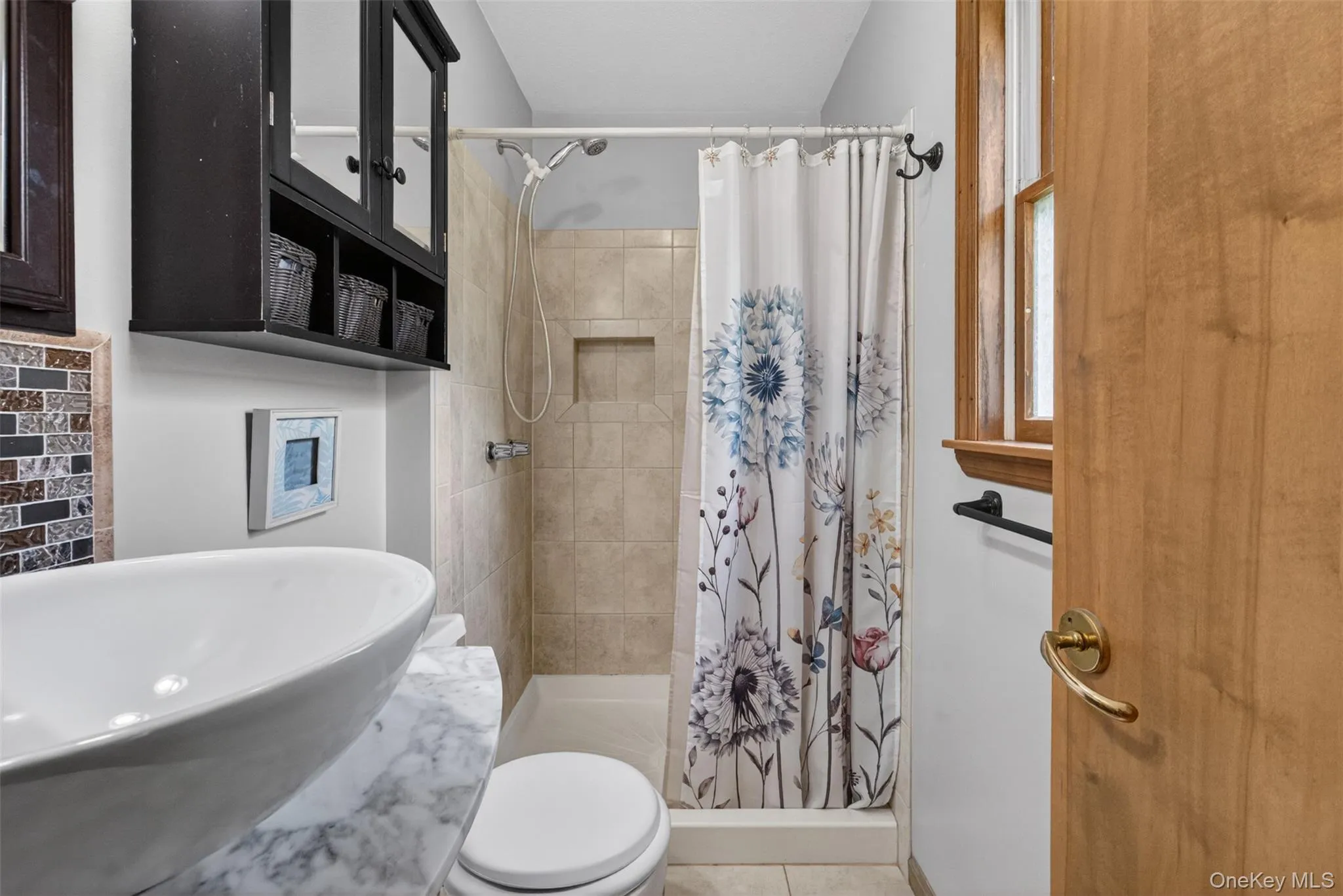Bathroom featuring a vessel sink on a marble-finish countertop, a dark wood-finish wall cabinet, and a tiled shower with a built-in niche Bathroom featuring a vessel sink on a marble-finish countertop, a dark wood-finish wall cabinet, and a tiled shower with a built-in niche