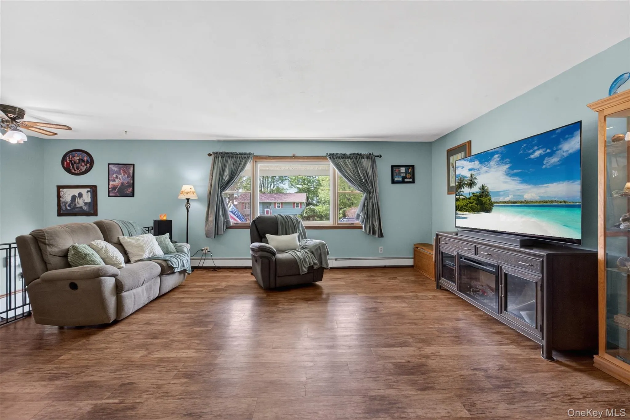 Spacious living area featuring wood-finish flooring, a large picture window, and a ceiling fan Spacious living area featuring wood-finish flooring, a large picture window, and a ceiling fan
