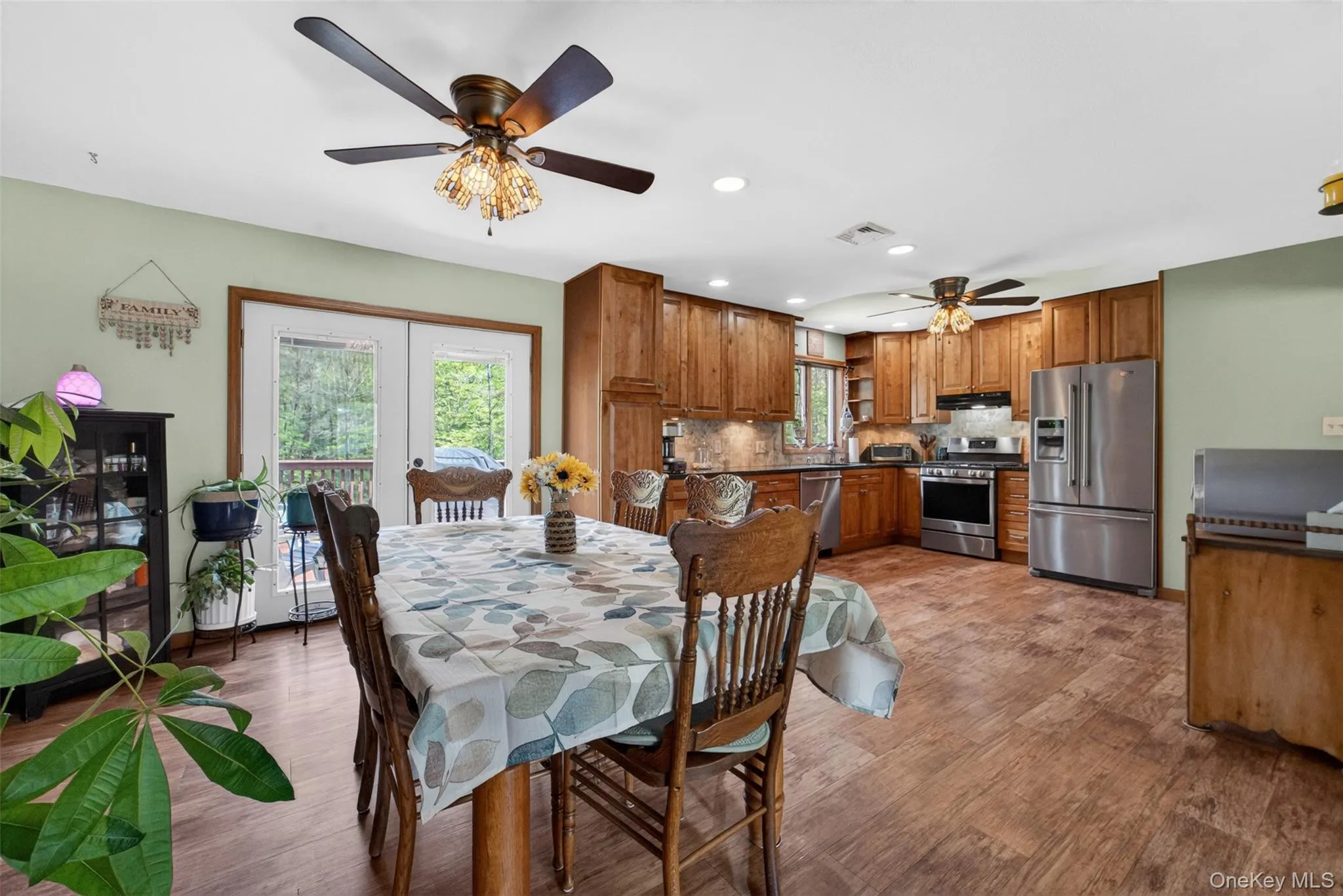 Open-concept kitchen and dining area featuring wood-finish flooring, custom wood cabinetry, stainless steel appliances, and a tile backsplash Open-concept kitchen and dining area featuring wood-finish flooring, custom wood cabinetry, stainless steel appliances, and a tile backsplash