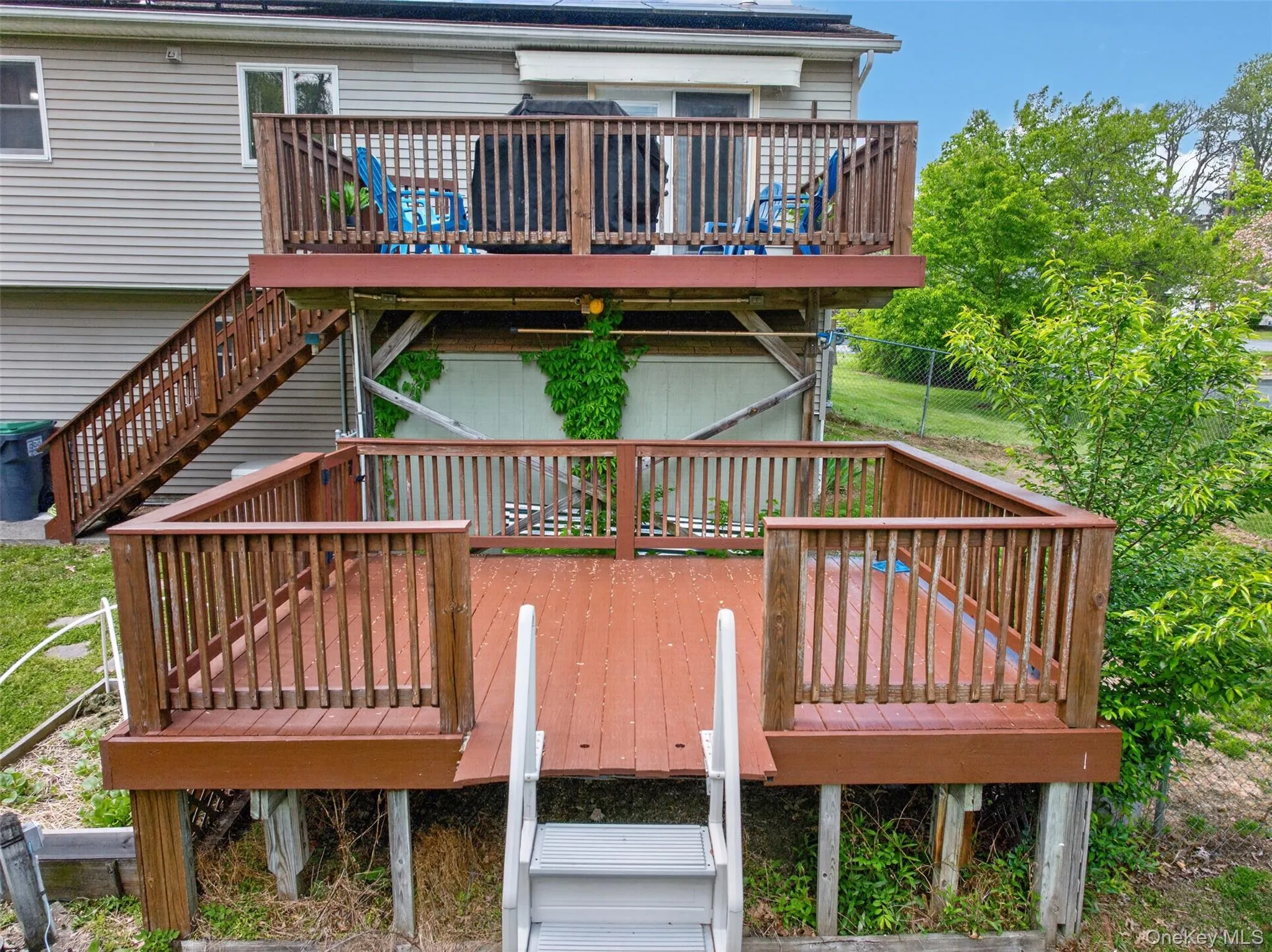 Two-tier wooden deck system featuring a lower-level deck with white steps use to be used for pool and an upper-level deck accessible via a dedicated staircase Two-tier wooden deck system featuring a lower-level deck with white steps use to be used for pool and an upper-level deck accessible via a dedicated staircase