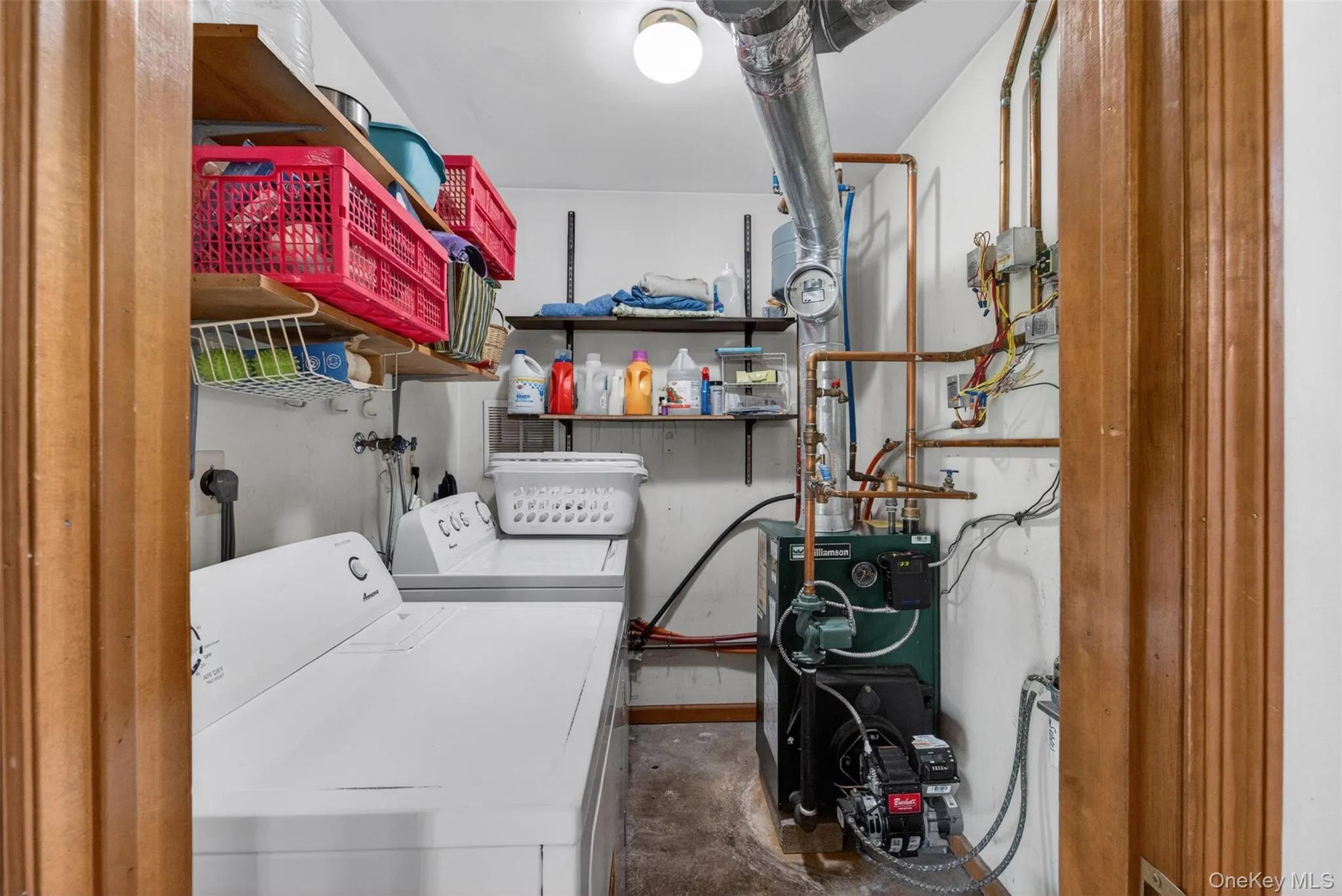 Utility room featuring laundry appliances, exposed copper piping, 7 year old Oil Burning Furnace, and built-in shelving Utility room featuring laundry appliances, exposed copper piping, 7 year old Oil Burning Furnace, and built-in shelving