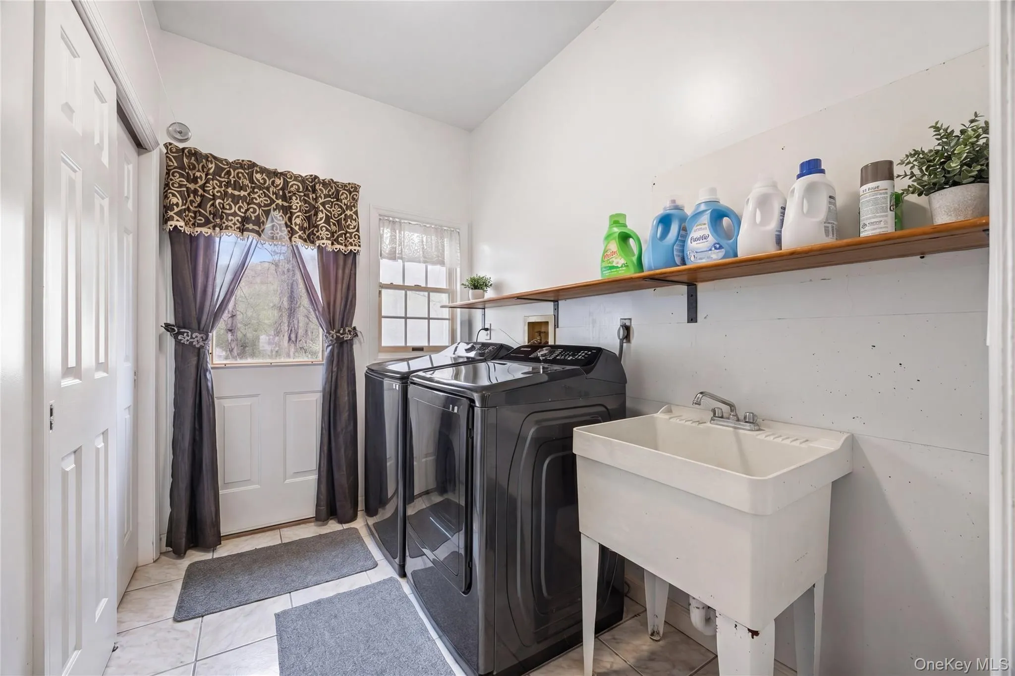 Dedicated laundry area featuring tile flooring, a utility sink, and a high-mounted wood-finish shelf Dedicated laundry area featuring tile flooring, a utility sink, and a high-mounted wood-finish shelf