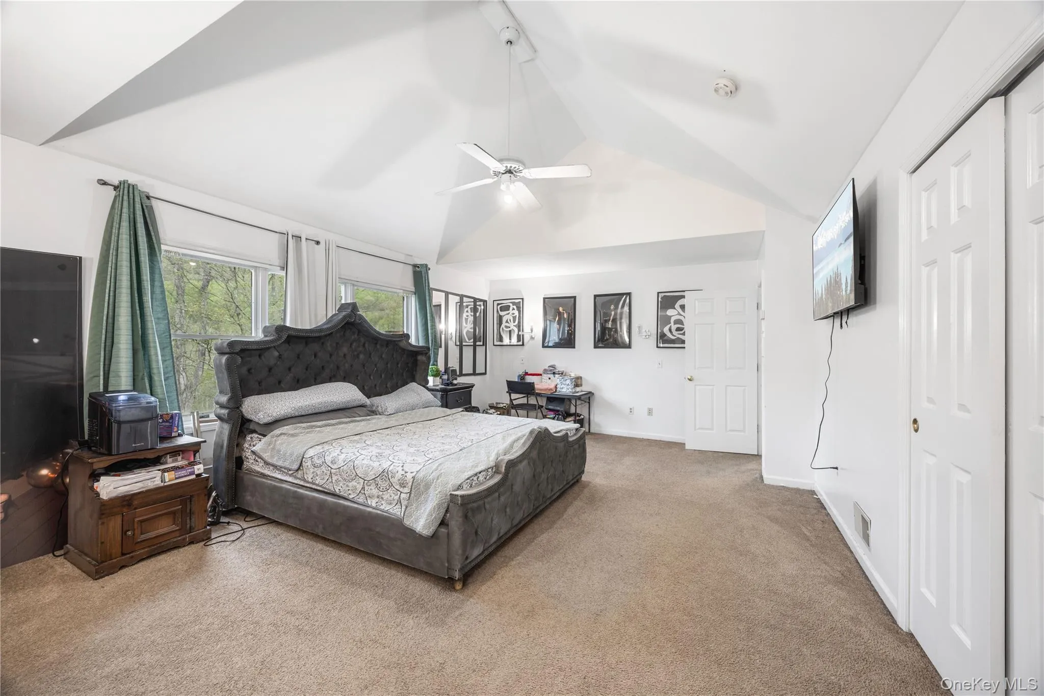Carpeted room featuring a vaulted ceiling with a ceiling fan, multiple windows with natural light, and paneled doors Carpeted room featuring a vaulted ceiling with a ceiling fan, multiple windows with natural light, and paneled doors