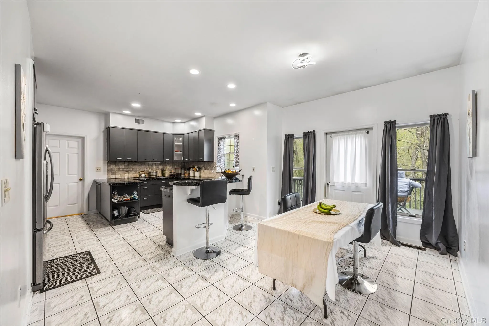 Open-concept kitchen with dark cabinetry, integrated island with counter seating, and tiled flooring Open-concept kitchen with dark cabinetry, integrated island with counter seating, and tiled flooring