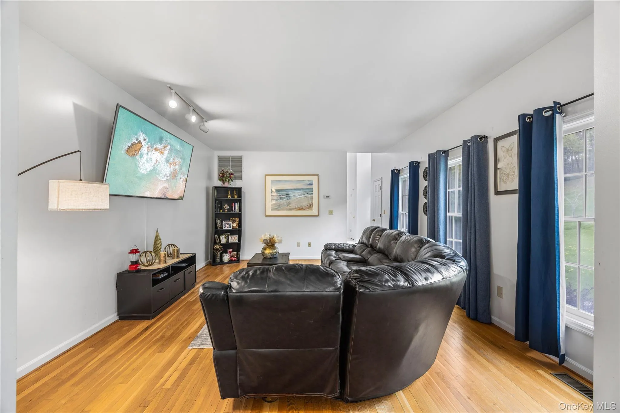 Spacious living area featuring vaulted ceilings, track lighting, wood-finish flooring, and multiple windows providing natural light Spacious living area featuring vaulted ceilings, track lighting, wood-finish flooring, and multiple windows providing natural light