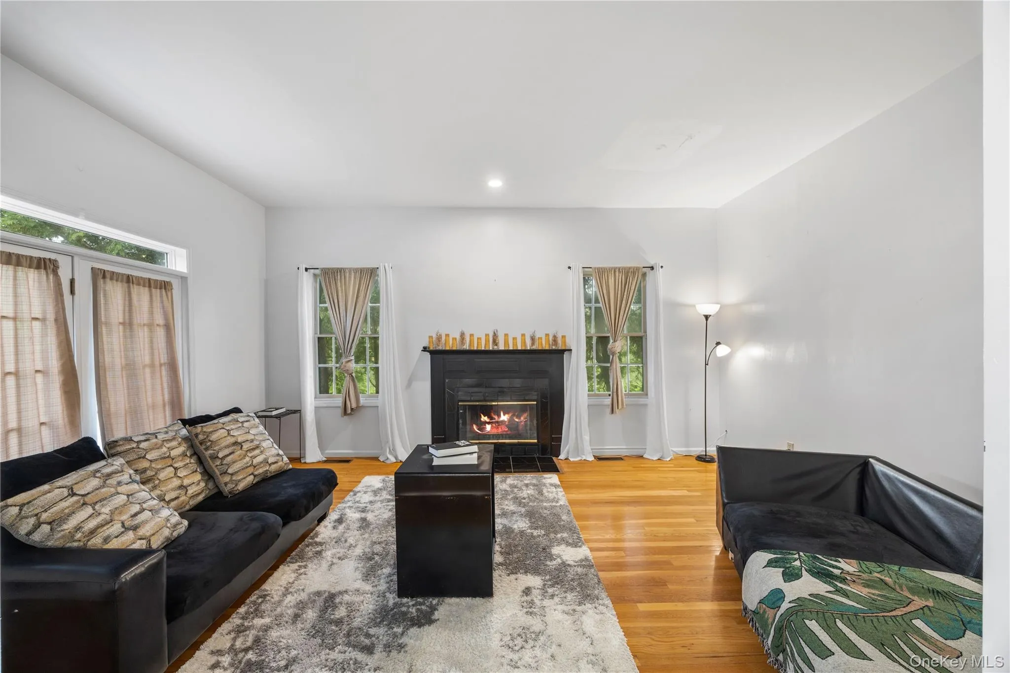 Living space featuring natural wood-finish flooring, a black mantle fireplace with a dark tile surround, and recessed ceiling lighting Living space featuring natural wood-finish flooring, a black mantle fireplace with a dark tile surround, and recessed ceiling lighting