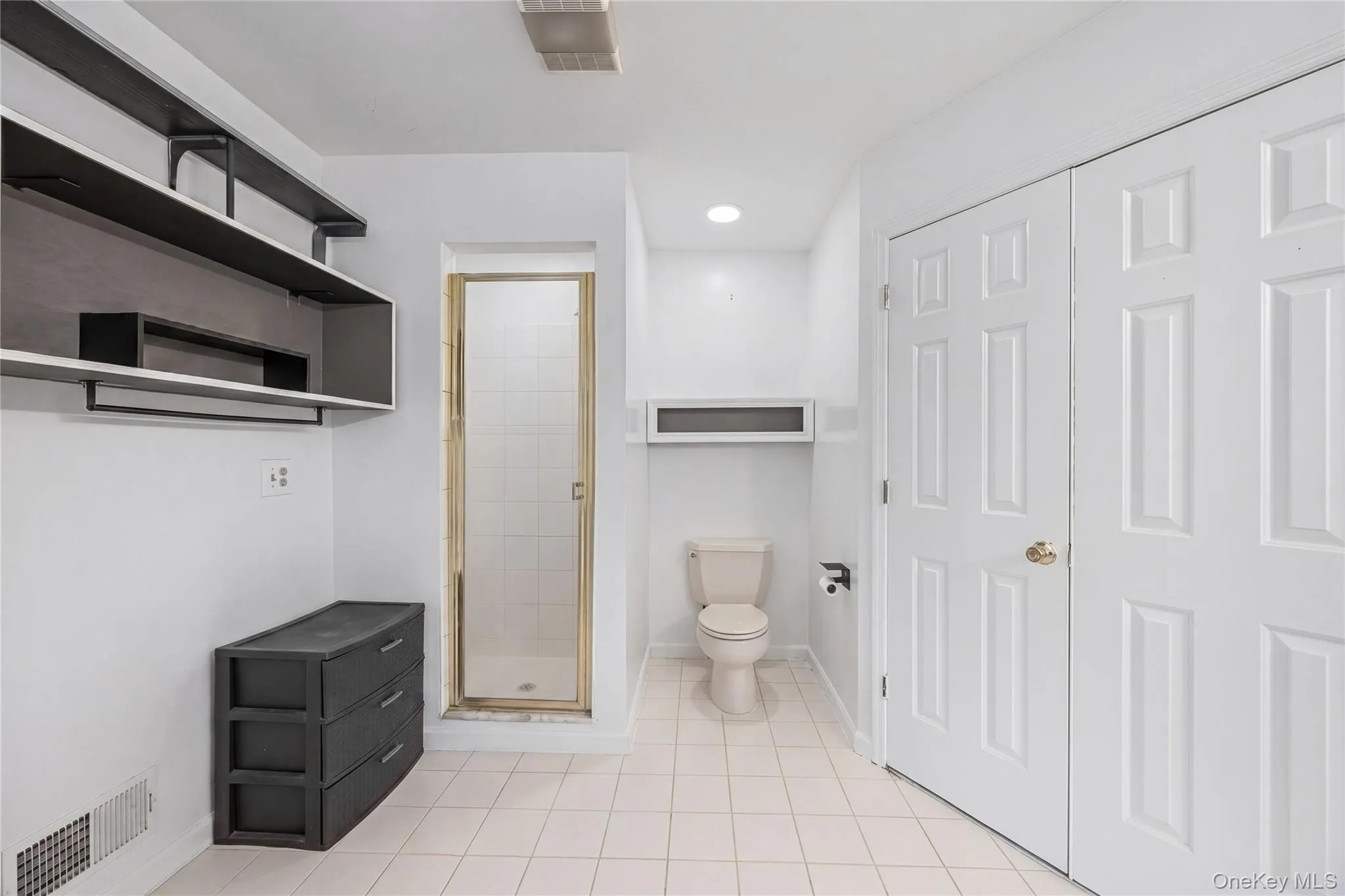 Bathroom featuring a tile-surround shower with glass door, white tile flooring, and a white toilet Bathroom featuring a tile-surround shower with glass door, white tile flooring, and a white toilet