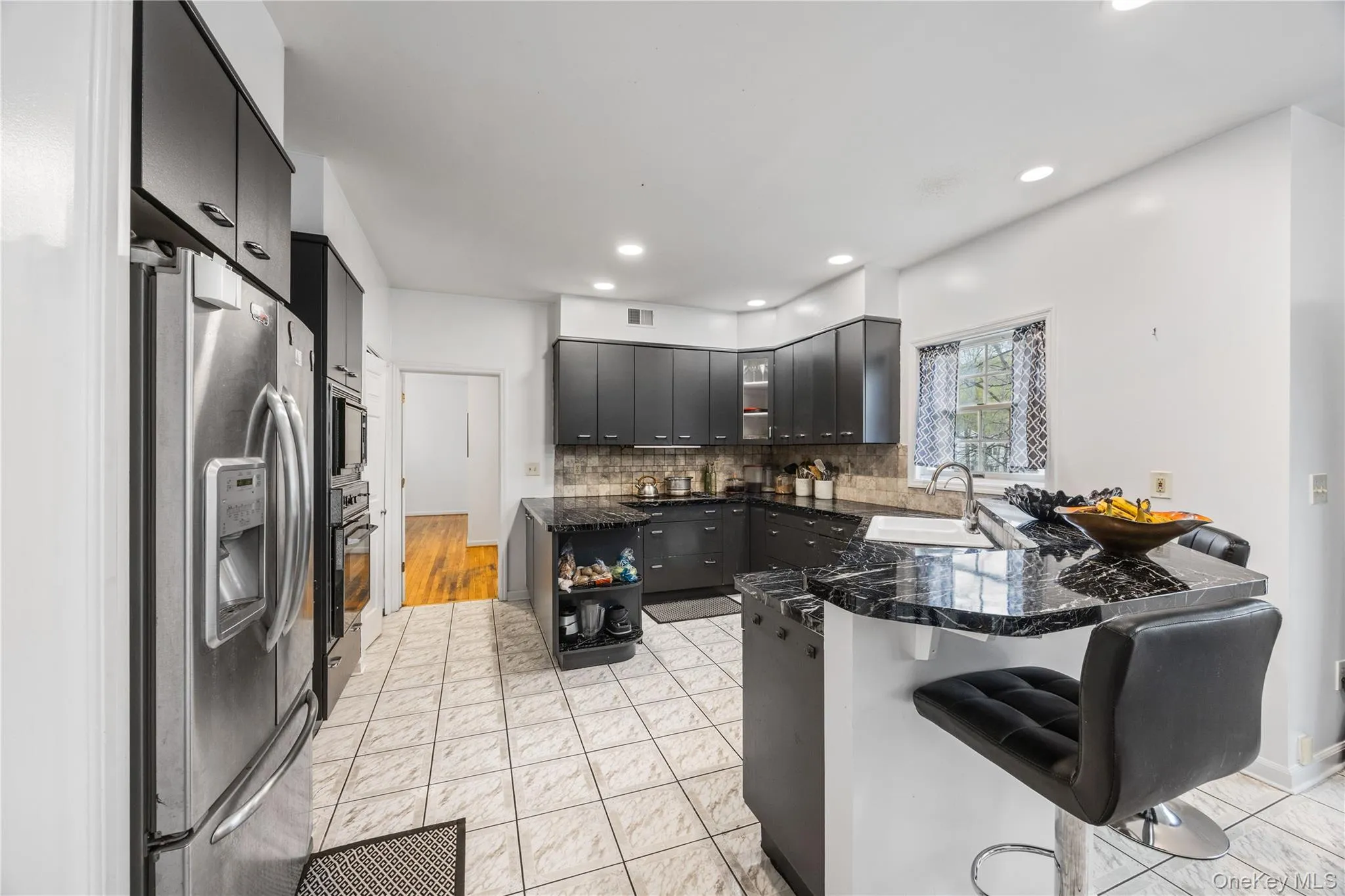 Kitchen featuring black cabinetry, stainless steel appliances, dark stone countertops, a breakfast bar with seating, and tiled flooring Kitchen featuring black cabinetry, stainless steel appliances, dark stone countertops, a breakfast bar with seating, and tiled flooring