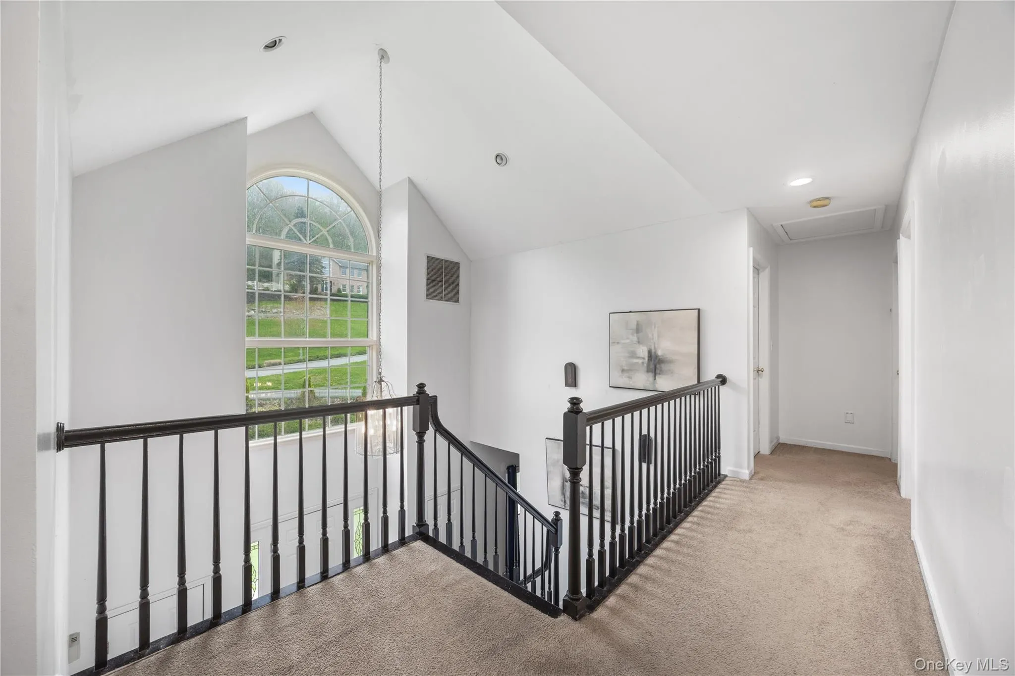 Vaulted ceiling entryway featuring a large arched window with grid details, a black wood baluster railing, recessed lighting, and carpeted flooring Vaulted ceiling entryway featuring a large arched window with grid details, a black wood baluster railing, recessed lighting, and carpeted flooring