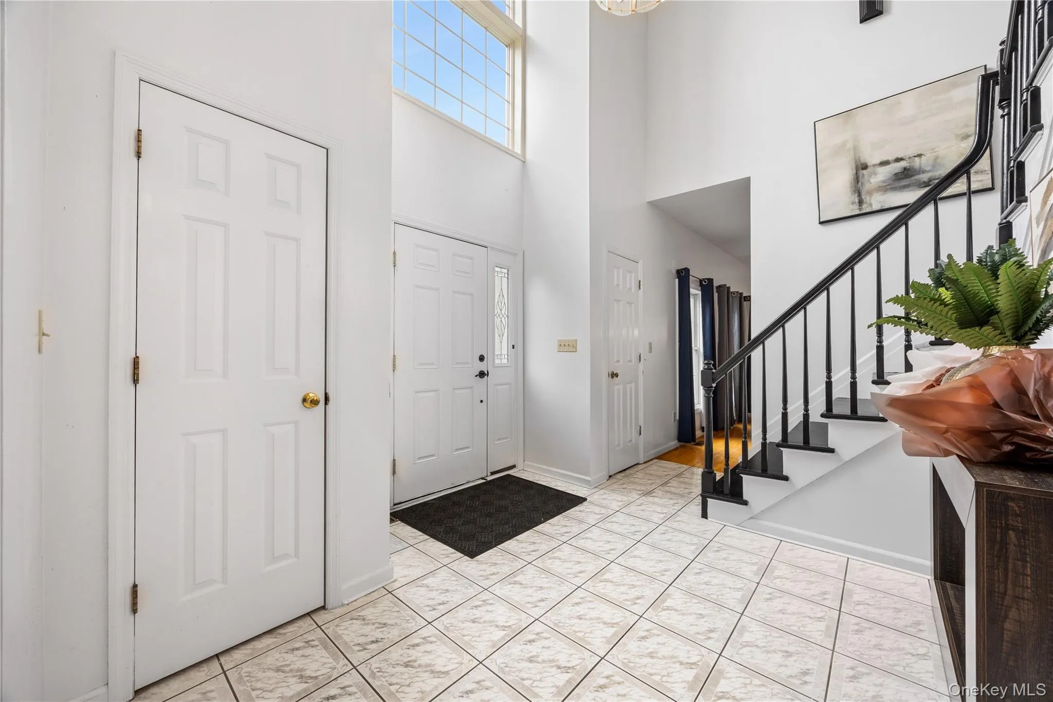 Two-story foyer with ceramic tile flooring, a prominent staircase with black banister and treads, and a high window feature Two-story foyer with ceramic tile flooring, a prominent staircase with black banister and treads, and a high window feature