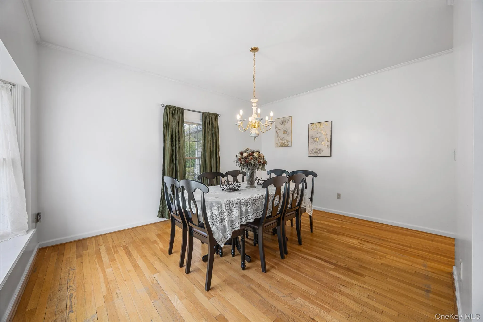 Dining area featuring natural wood-finish flooring, white walls, and a brass-tone chandelier Dining area featuring natural wood-finish flooring, white walls, and a brass-tone chandelier